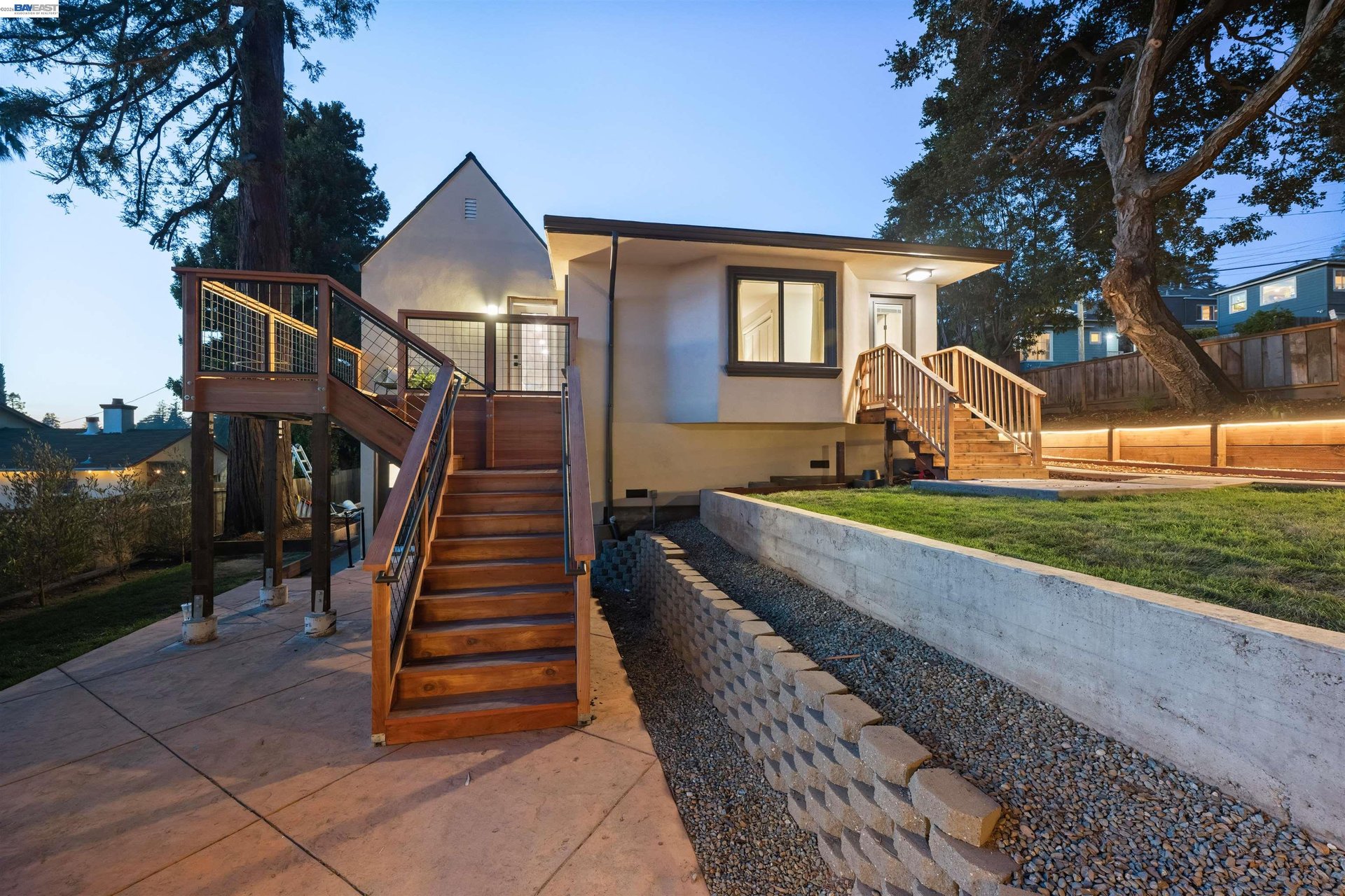Oakland home at dusk with broad wooden stairs, elevated decks, and a landscaped sloping yard.
