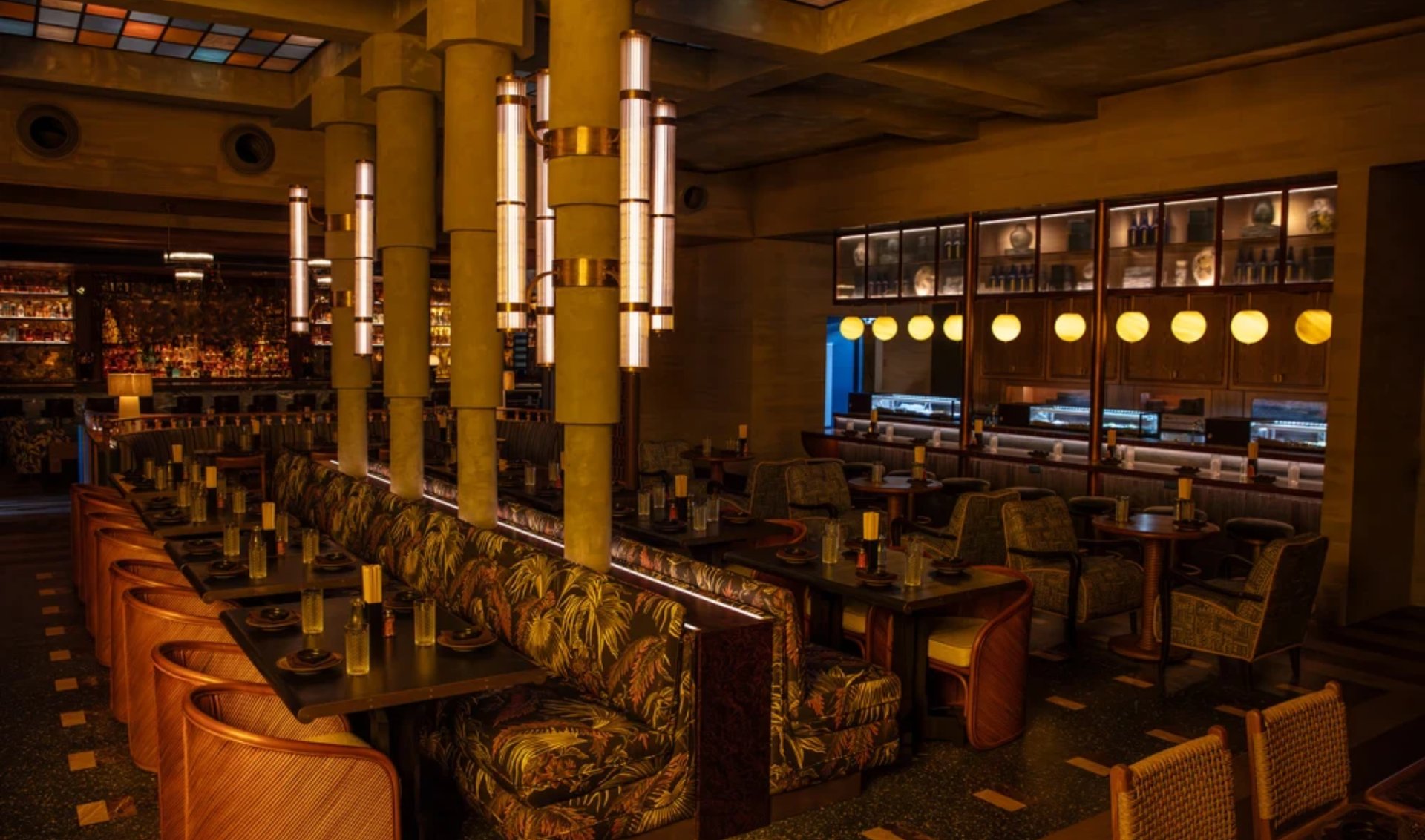 Upscale restaurant dining room with a floral banquette, rattan chairs, and warm pendant lighting.