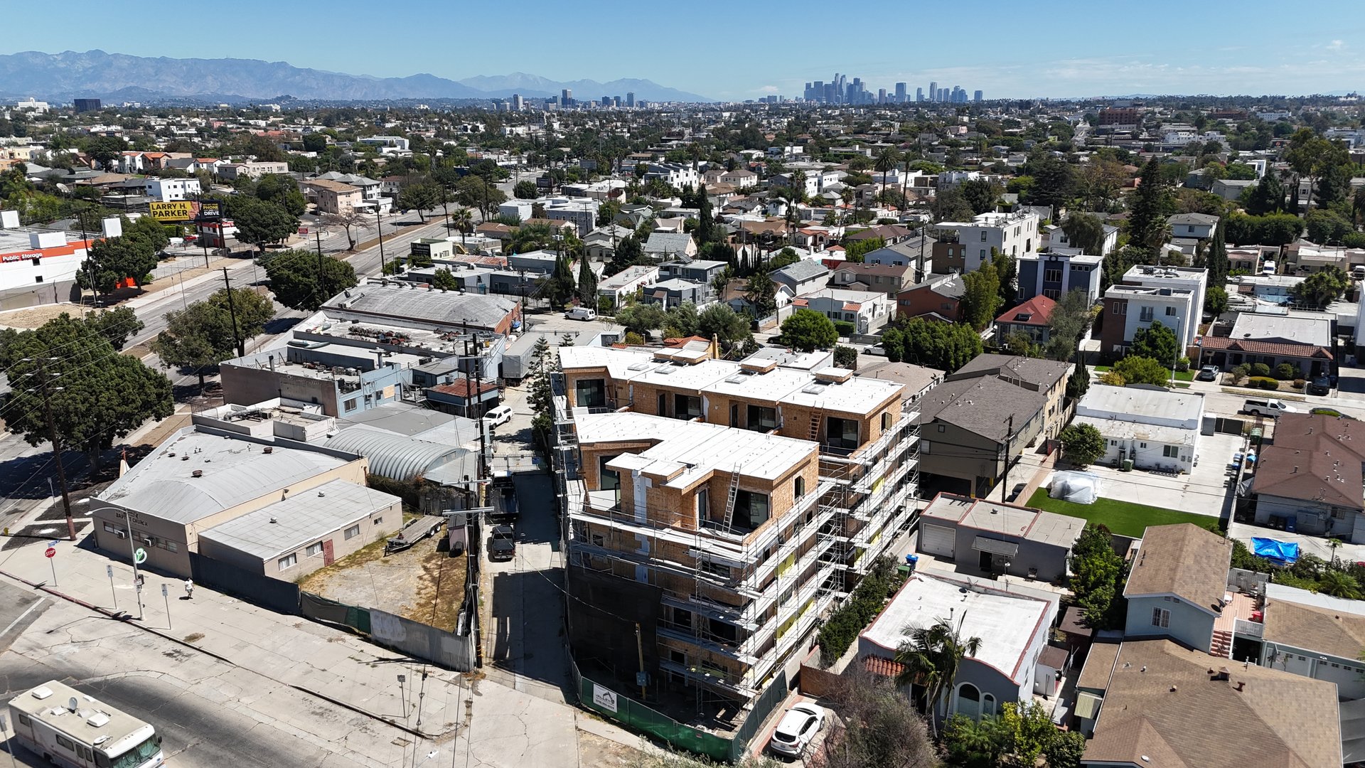Aerial view of a multi-story building under construction, with scaffolding and the Los Angeles skyline in the distance.