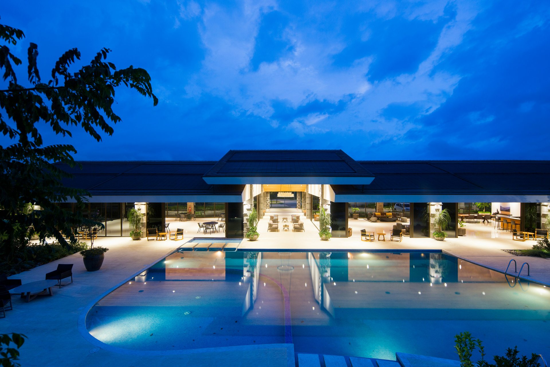 Contemporary venue with a large pool, illuminated seating areas, and open architecture under a deep blue evening sky.