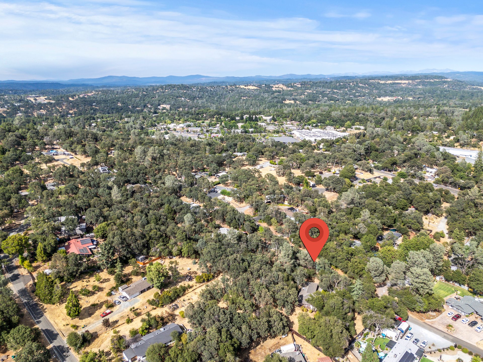 Aerial view of a wooded neighborhood, with a red pin marking the property and hills in the distance.