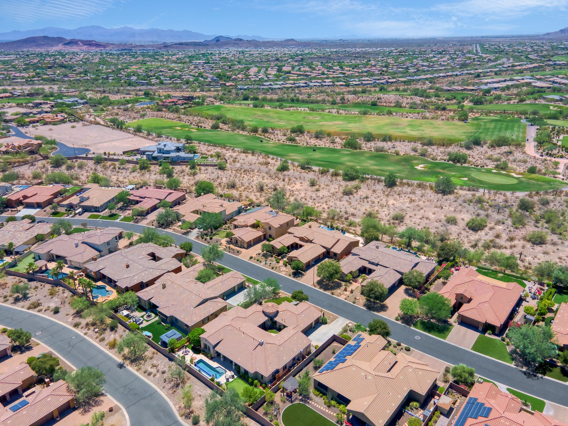 Aerial view of a suburban desert neighborhood beside a golf course with mountains in the distance.