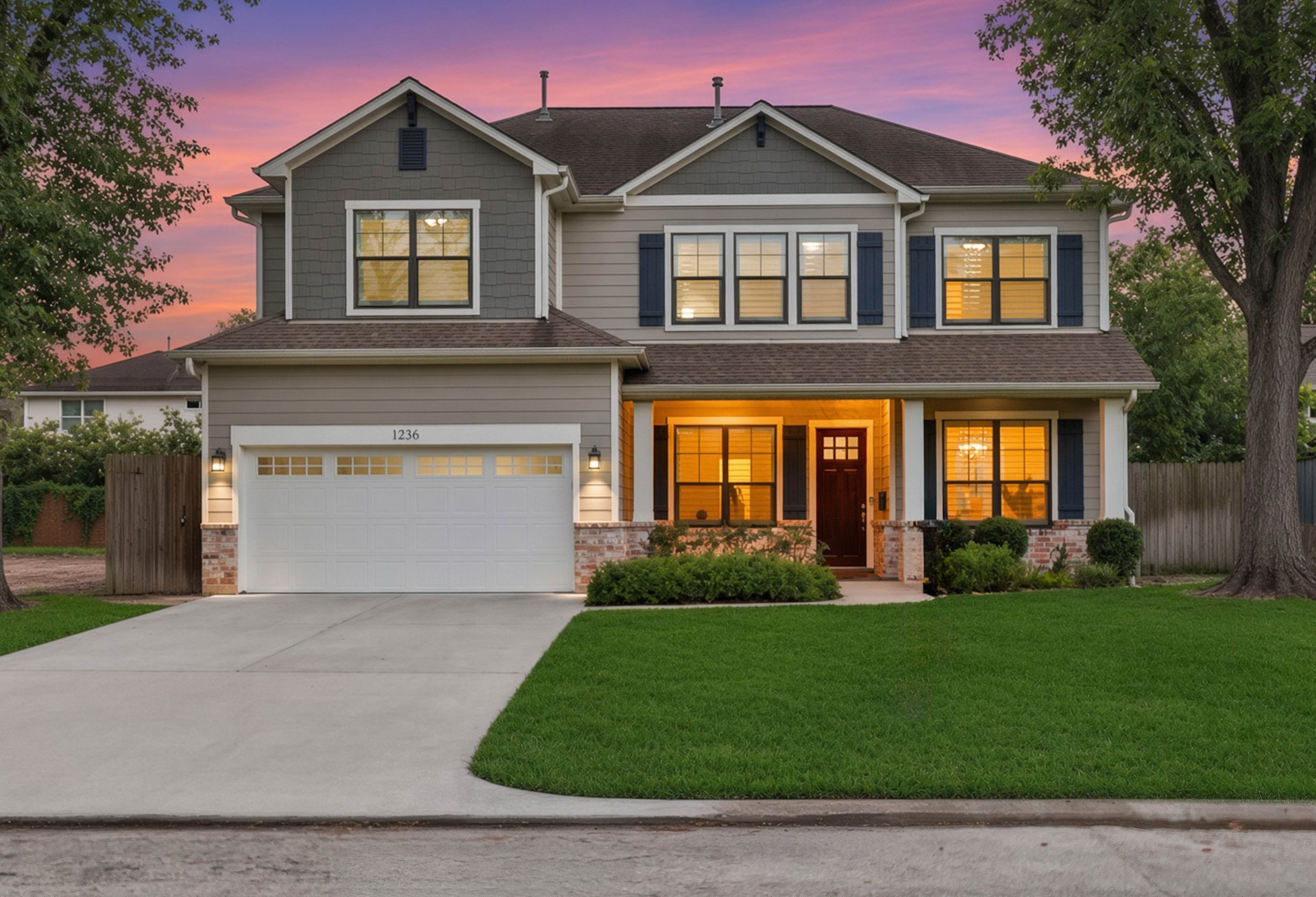Two-story gray house with blue shutters, a double garage, and warmly lit windows at dusk.