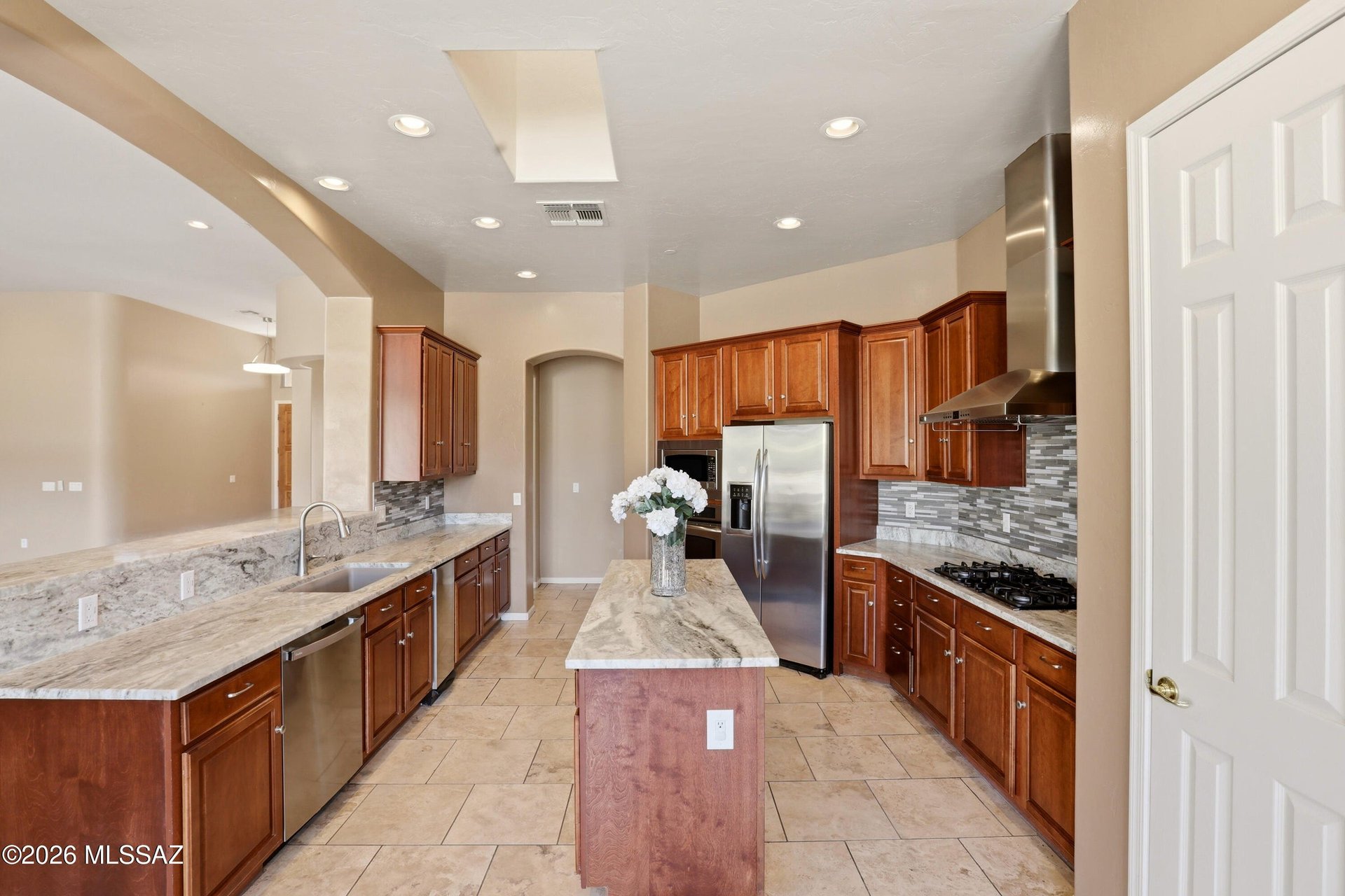 Kitchen with a central granite island, reddish wood cabinets, and stainless steel appliances.