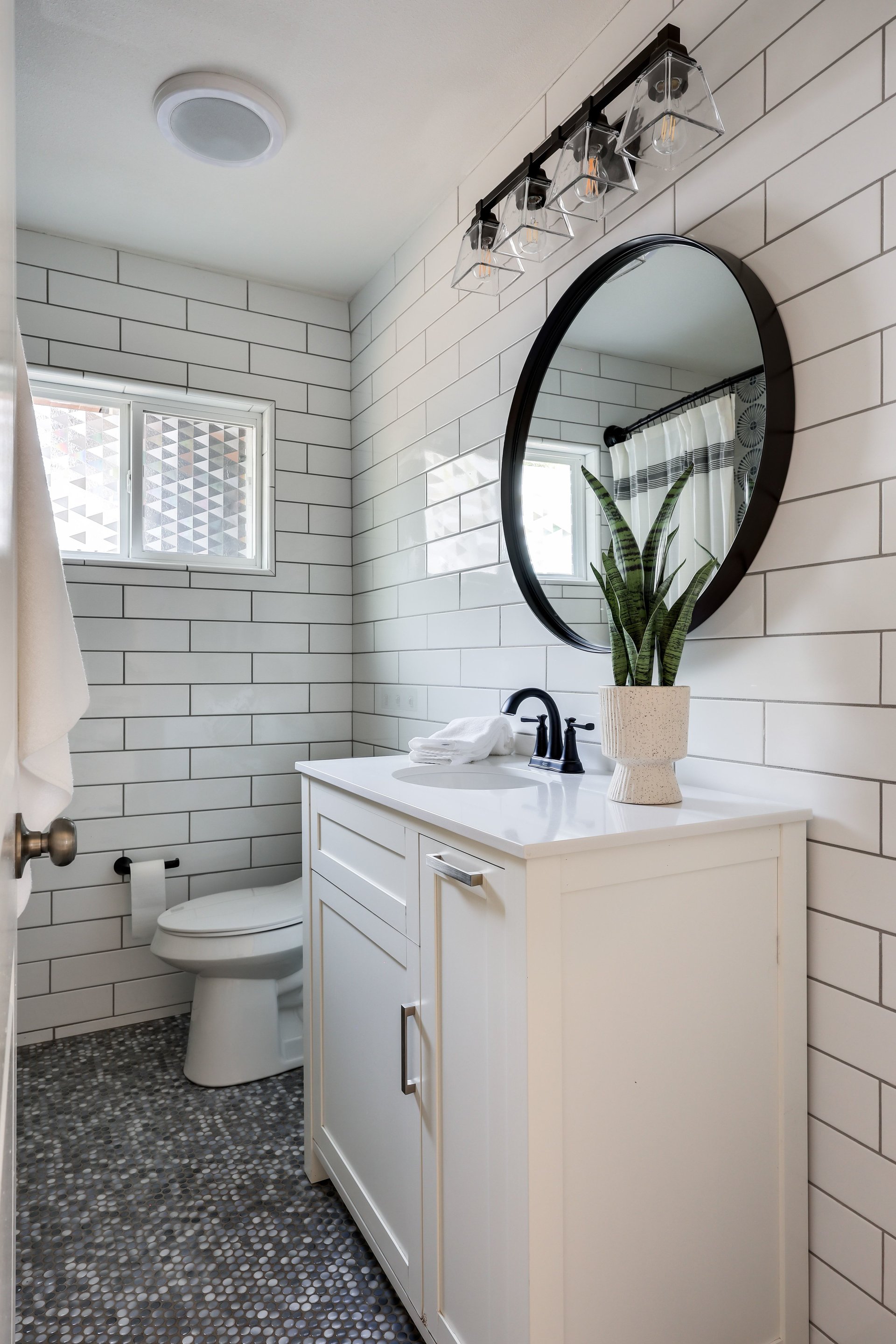 Bathroom with white subway tile, a round black-framed mirror, and a pebble-tile floor.