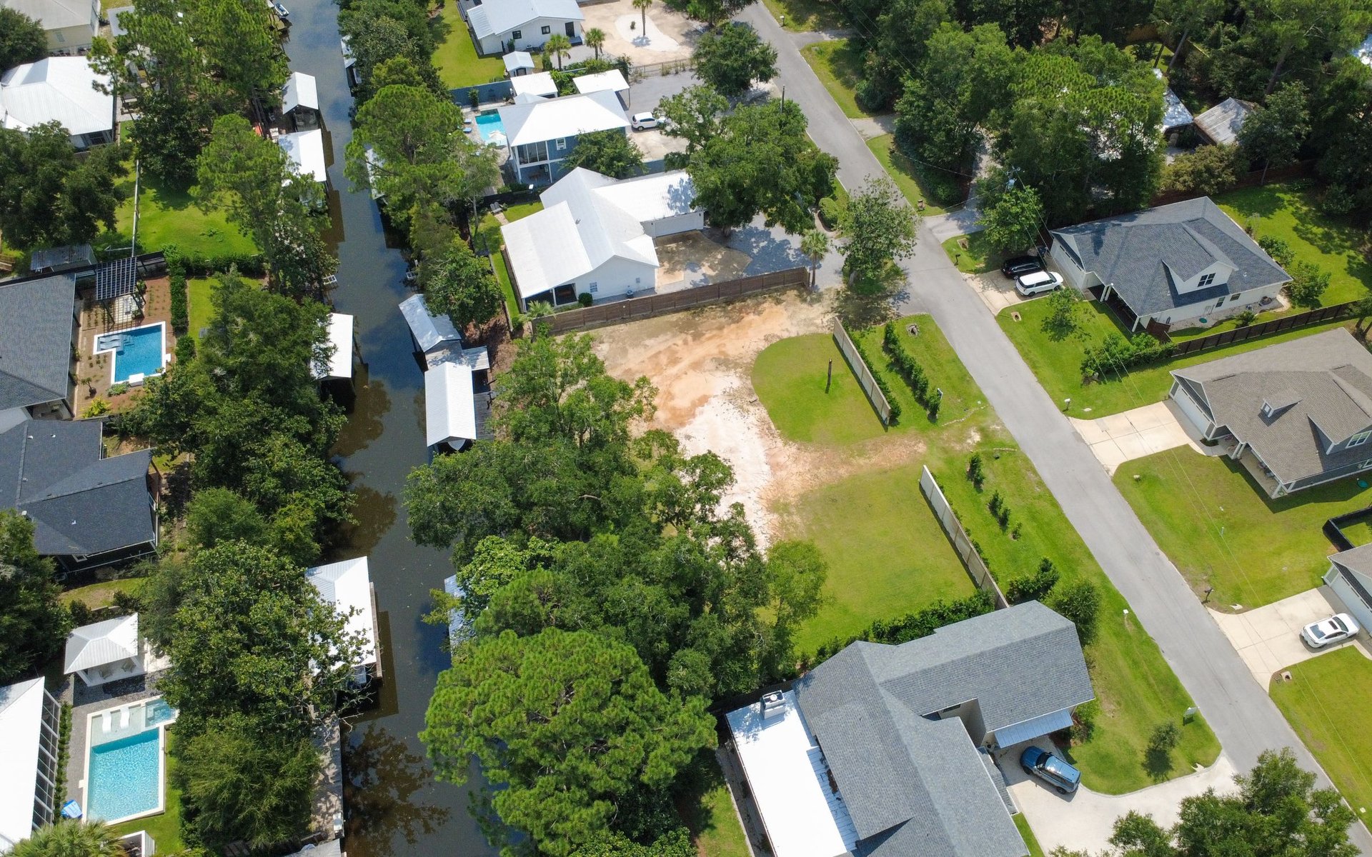 Cleared vacant lot beside a canal, surrounded by homes and trees.