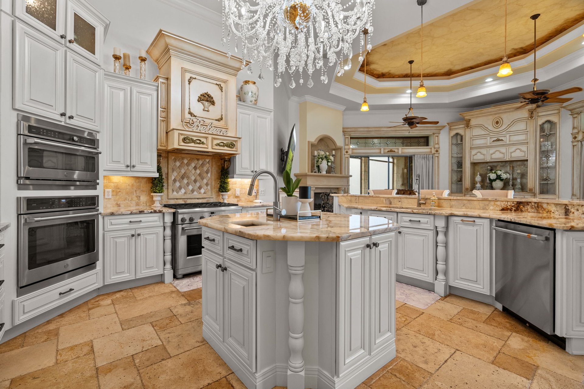 Ornate kitchen with a large stone island, white cabinetry, double ovens, and a crystal chandelier.