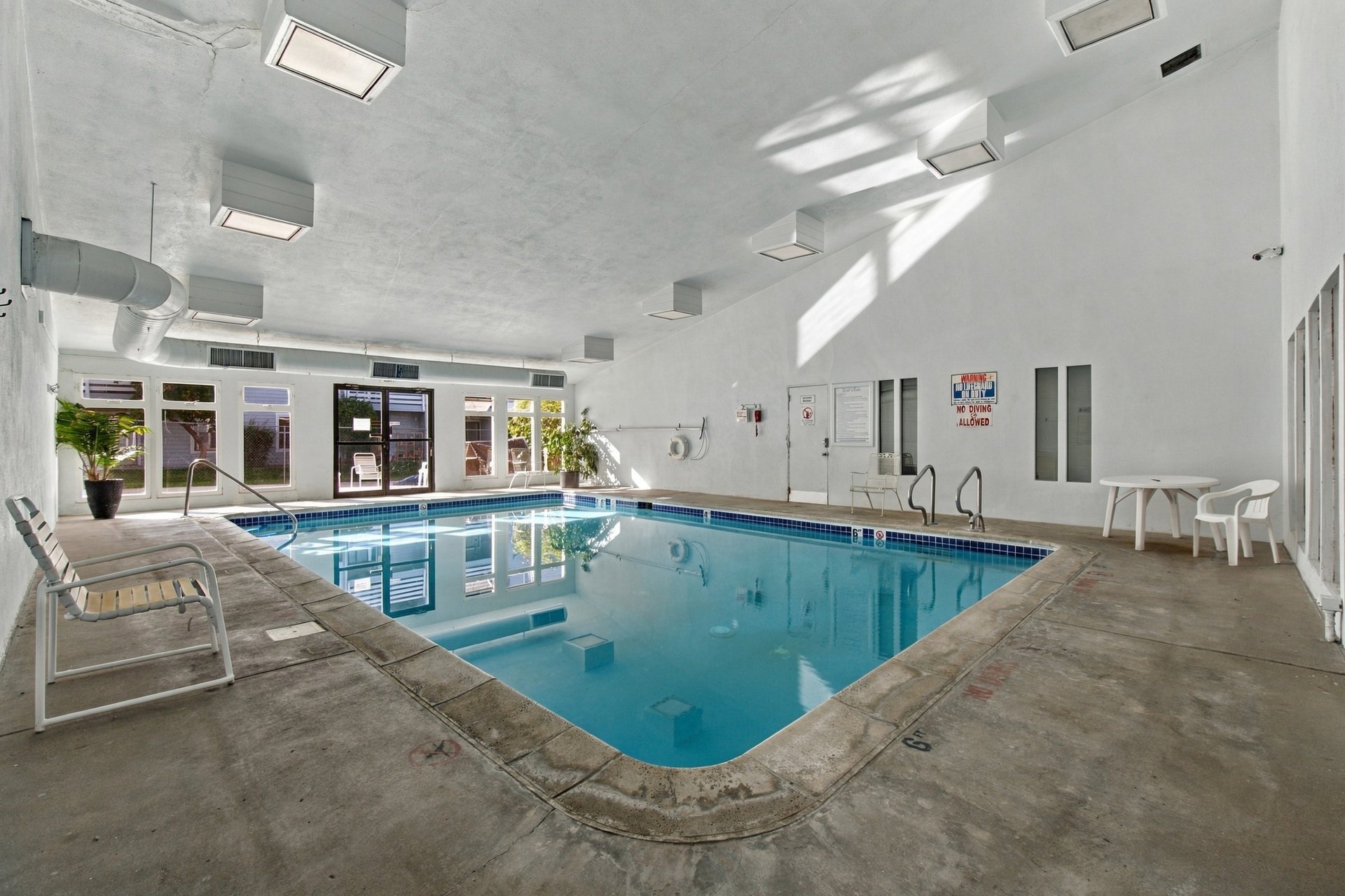 Indoor swimming pool with blue water, tiled edges, and lounge chairs along the deck.