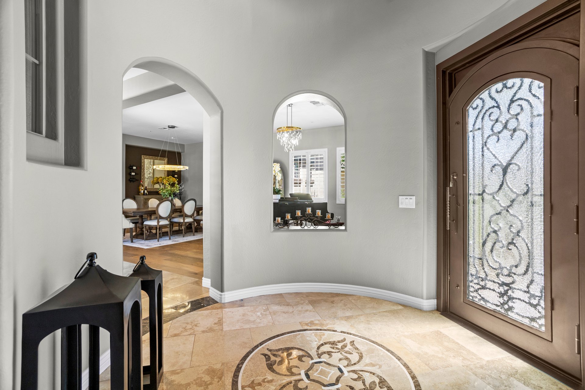Spacious front entry with arched openings, decorative tile floor, and a glass-paneled front door leading toward a dining room.