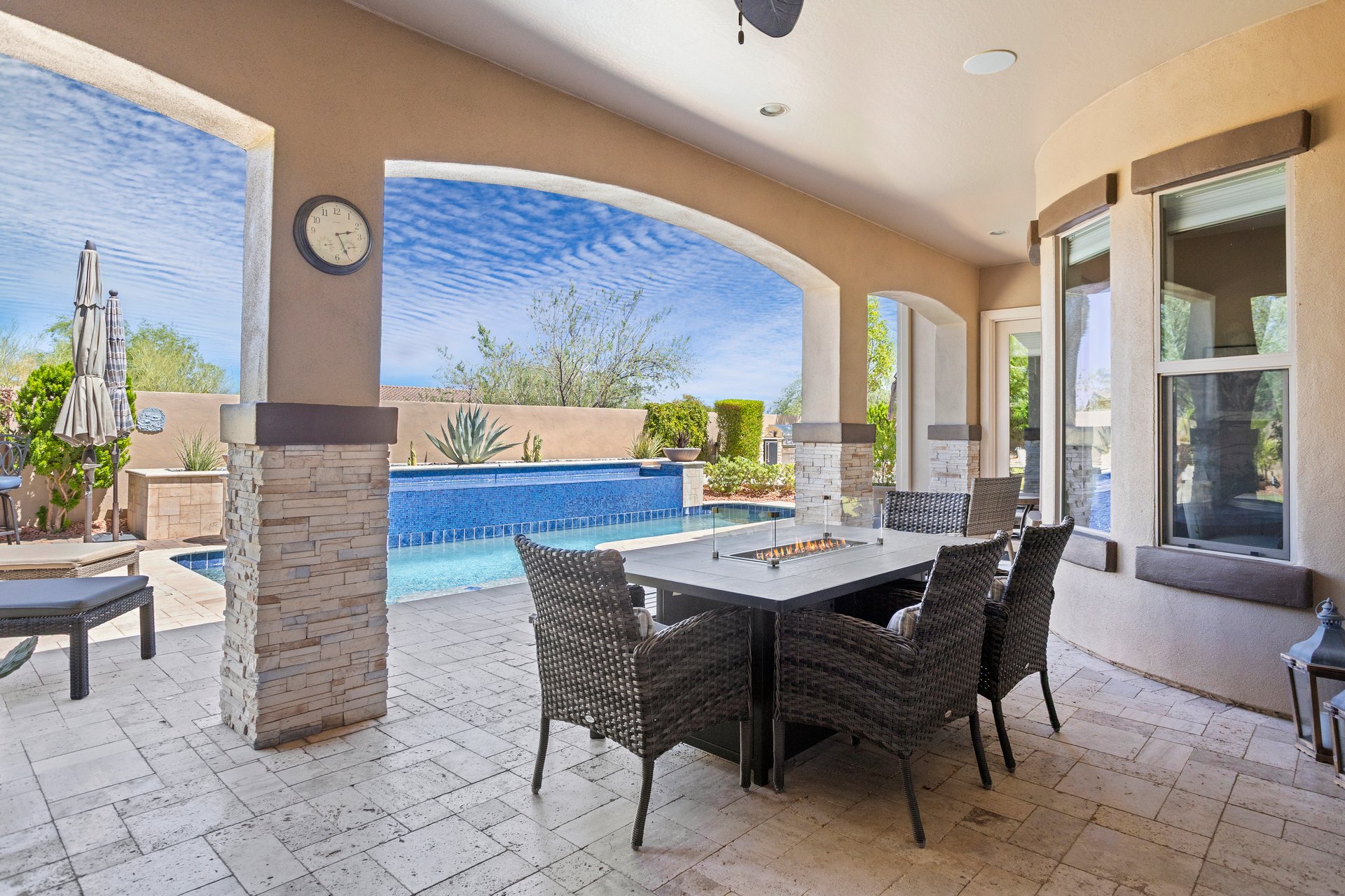 Covered outdoor patio with dining table and wicker chairs overlooking a pool and landscaped backyard.