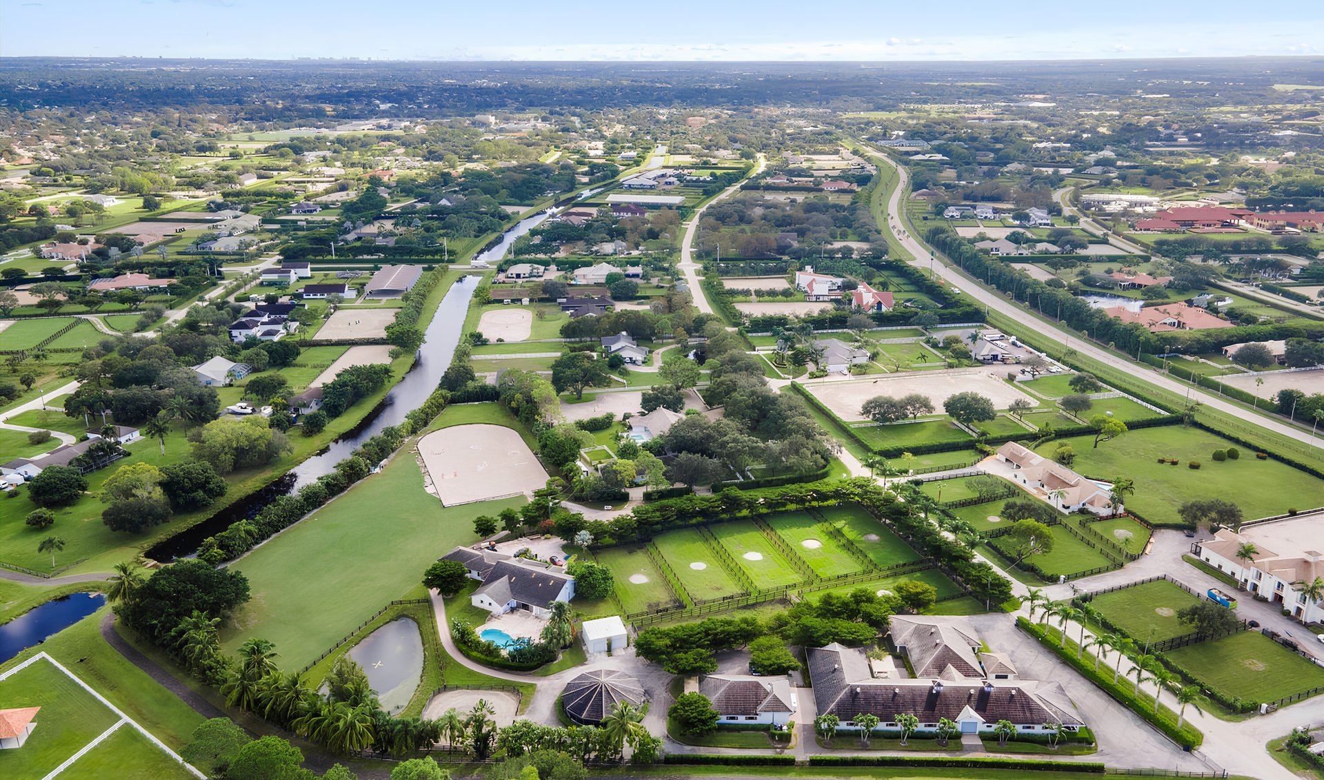Aerial view of an equestrian neighborhood with fenced paddocks, riding arenas, large homes, and a canal.