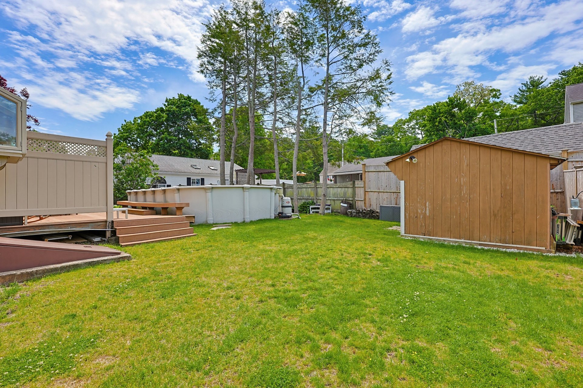 Fenced backyard with an above-ground pool beside a raised deck and wooden shed.
