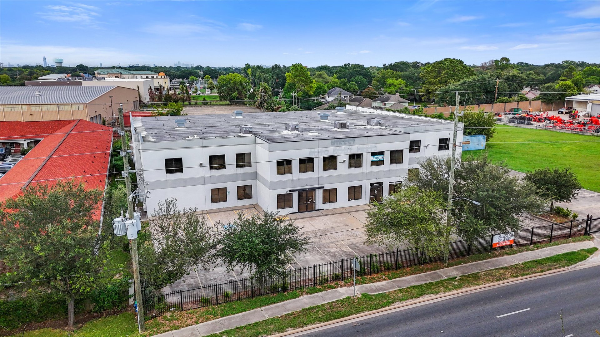 Aerial view of a two-story commercial building with a paved forecourt and fenced frontage.