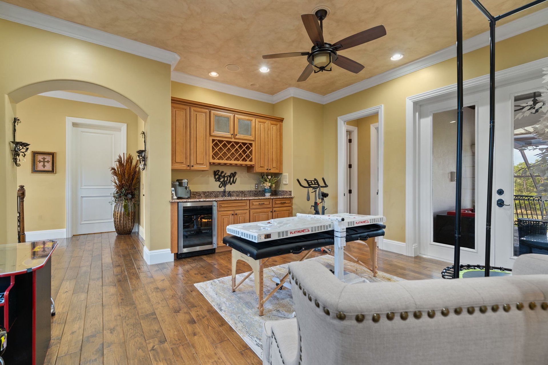 Furnished fitness and massage room with built-in cabinets, a massage table, exercise bike, and balcony doors.