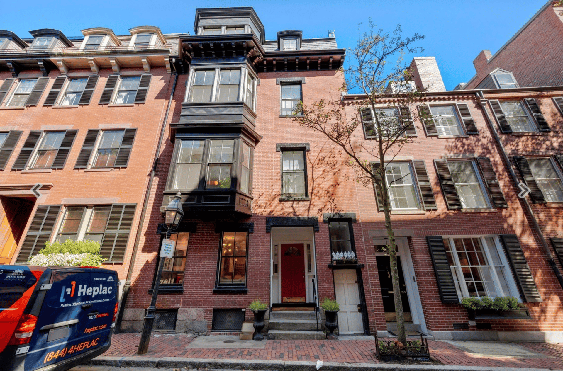 Red-brick townhouse with a prominent dark bay window, black shutters, and a red front door.