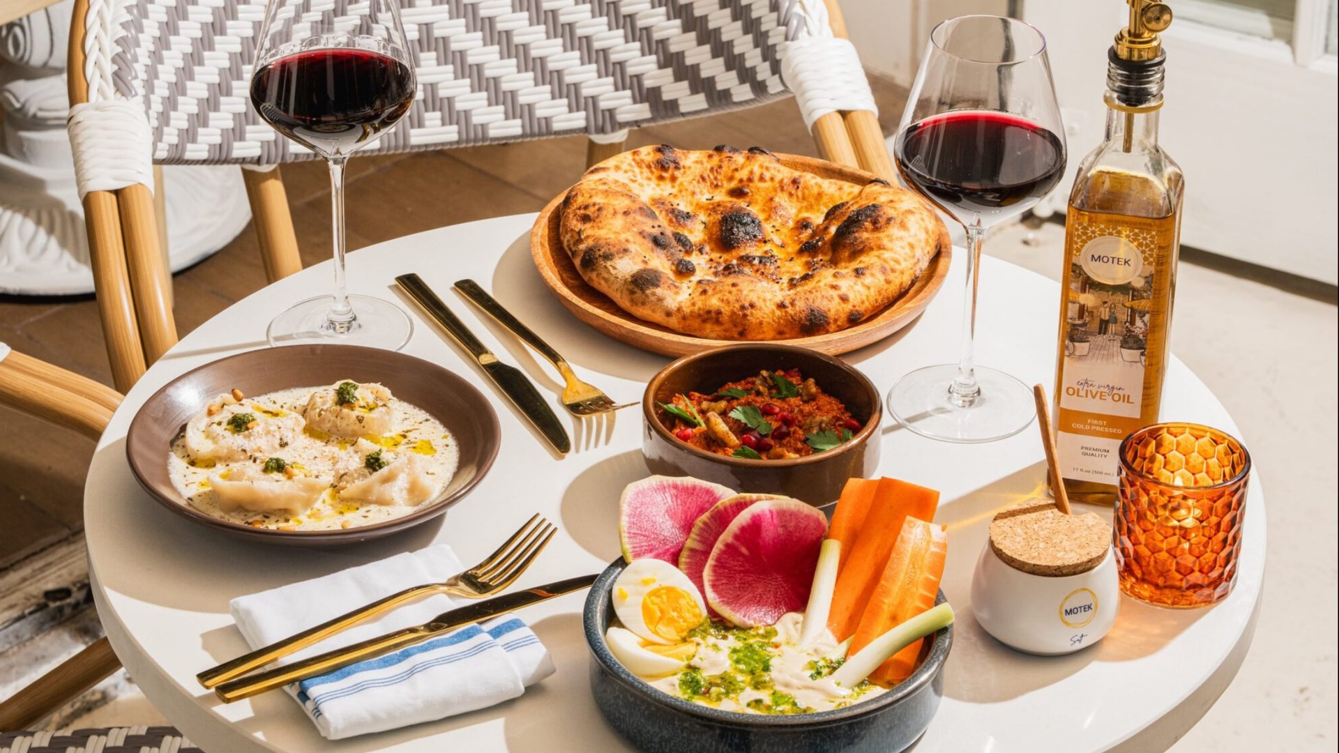 Mediterranean dining spread with wine glasses, hummus, flatbread, and colorful vegetable crudité platter
