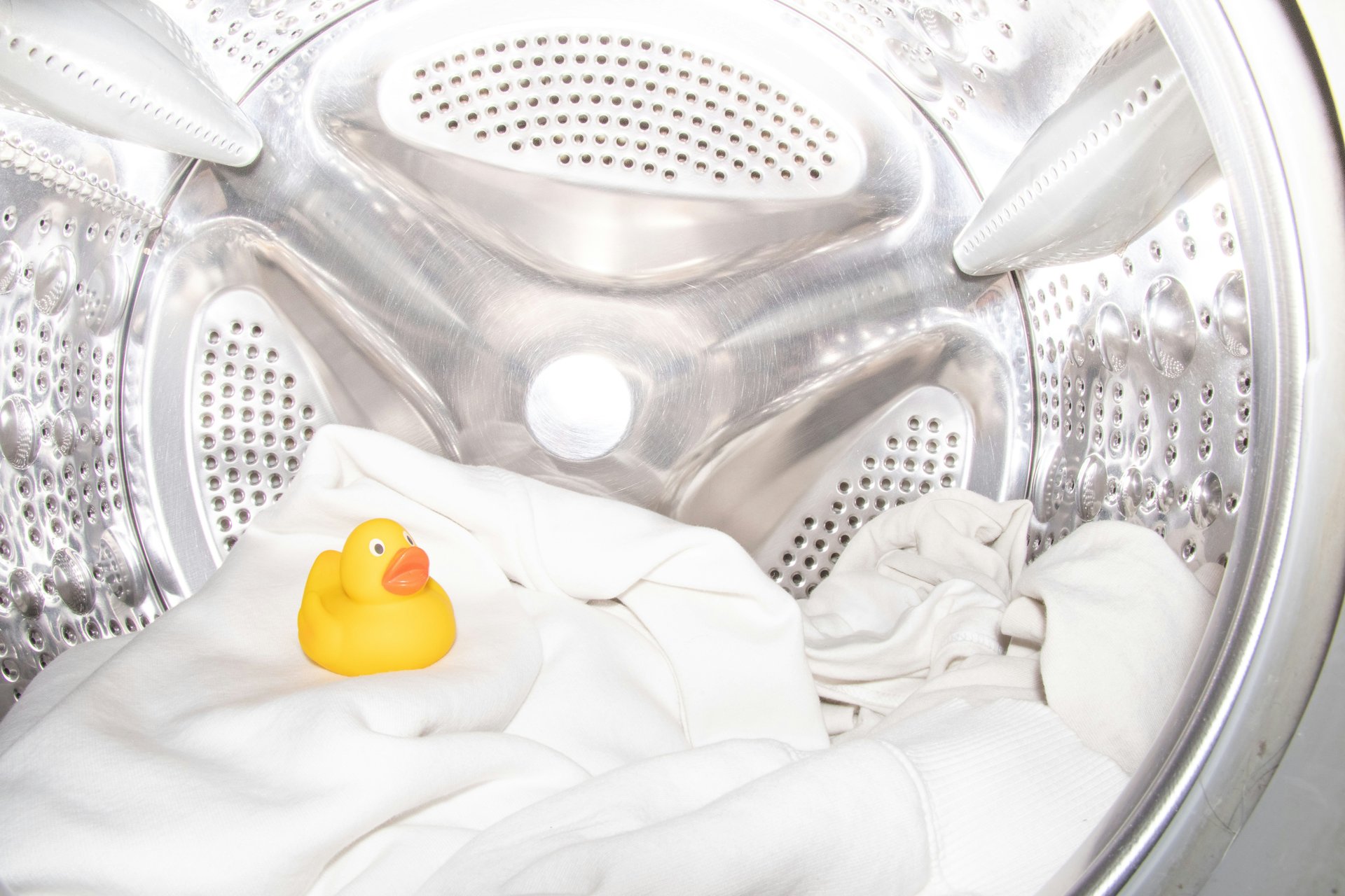 White laundry and a yellow rubber duck inside a metal dryer drum.