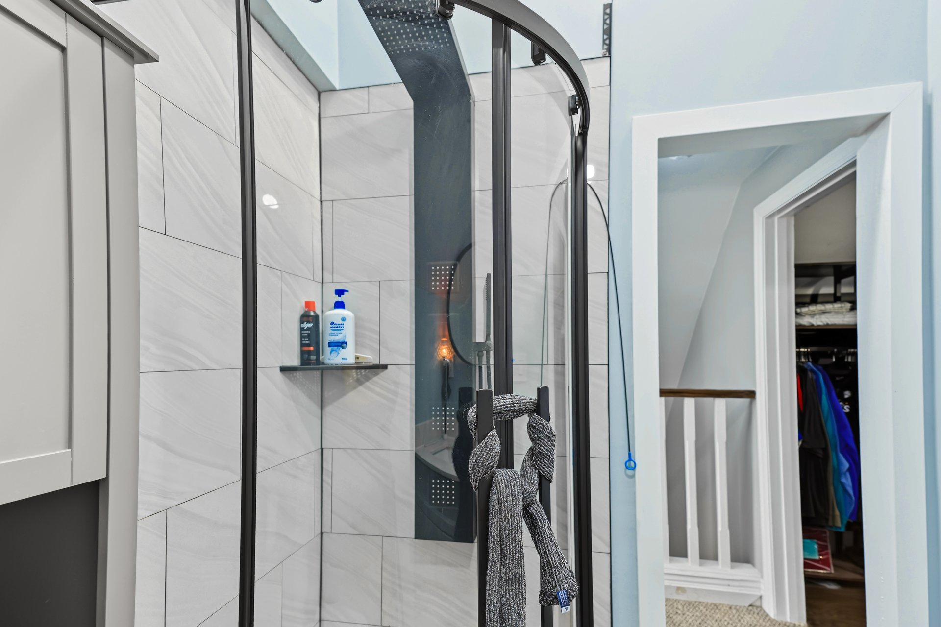 Bathroom shower with gray tile and dark shower panel beside an open closet.