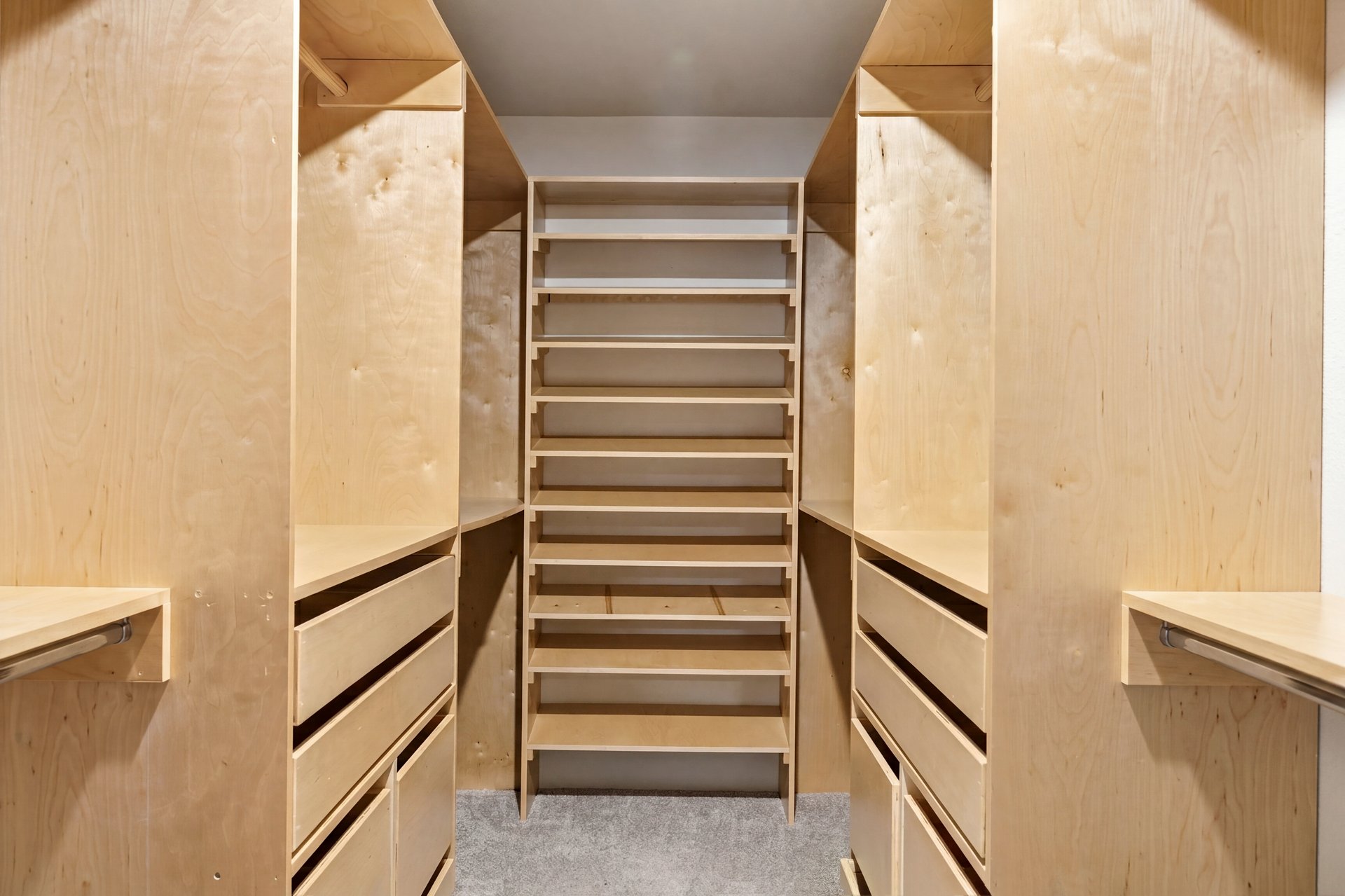 Walk-in closet with light wood built-in shelves, drawers, and hanging rods.
