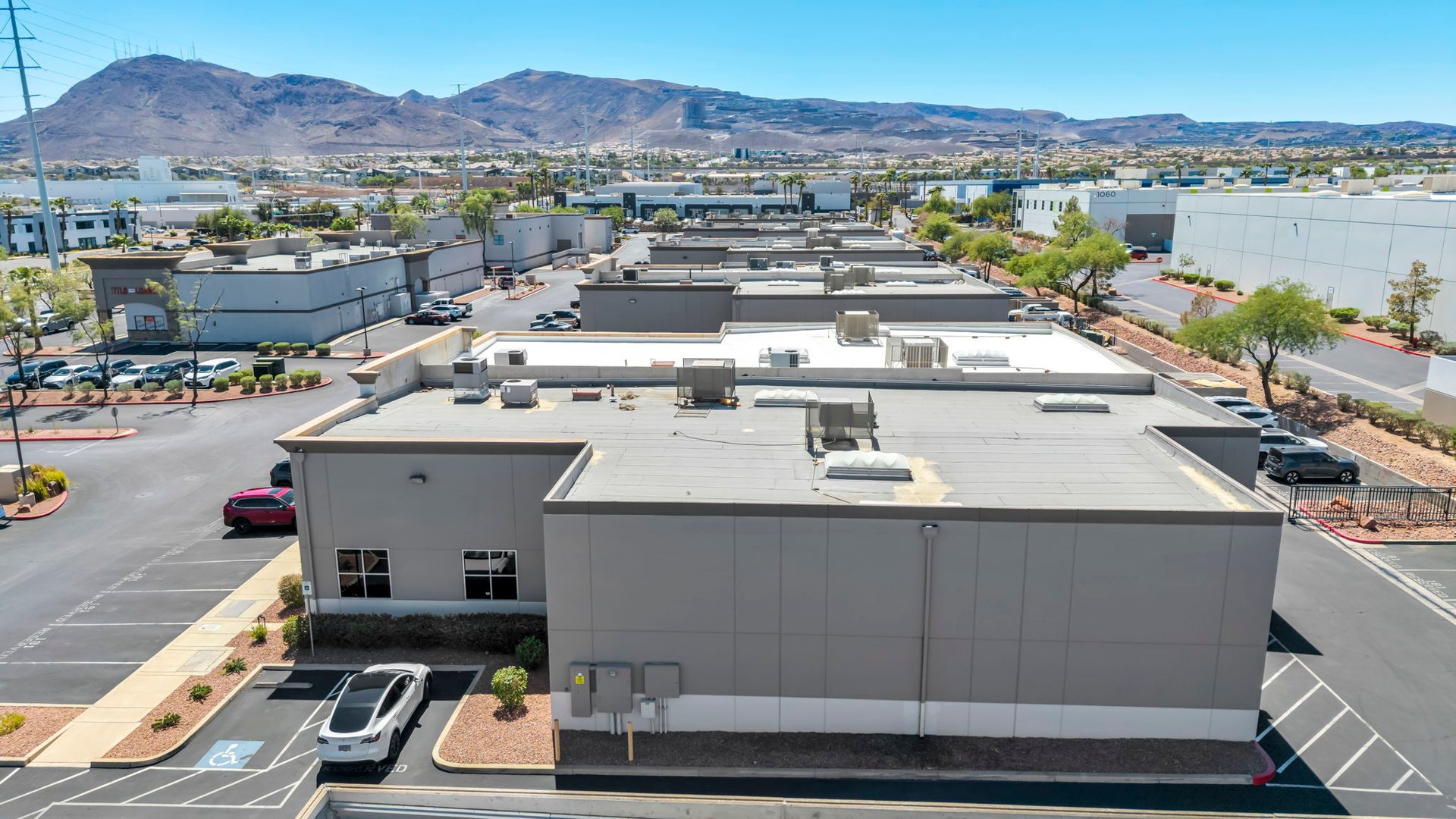 Commercial building with a broad flat roof, parking lots, and mountains in the distance.