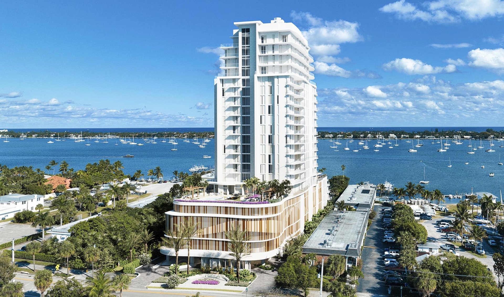Modern white condo tower beside a marina, with curved balconies and sailboats across the water.