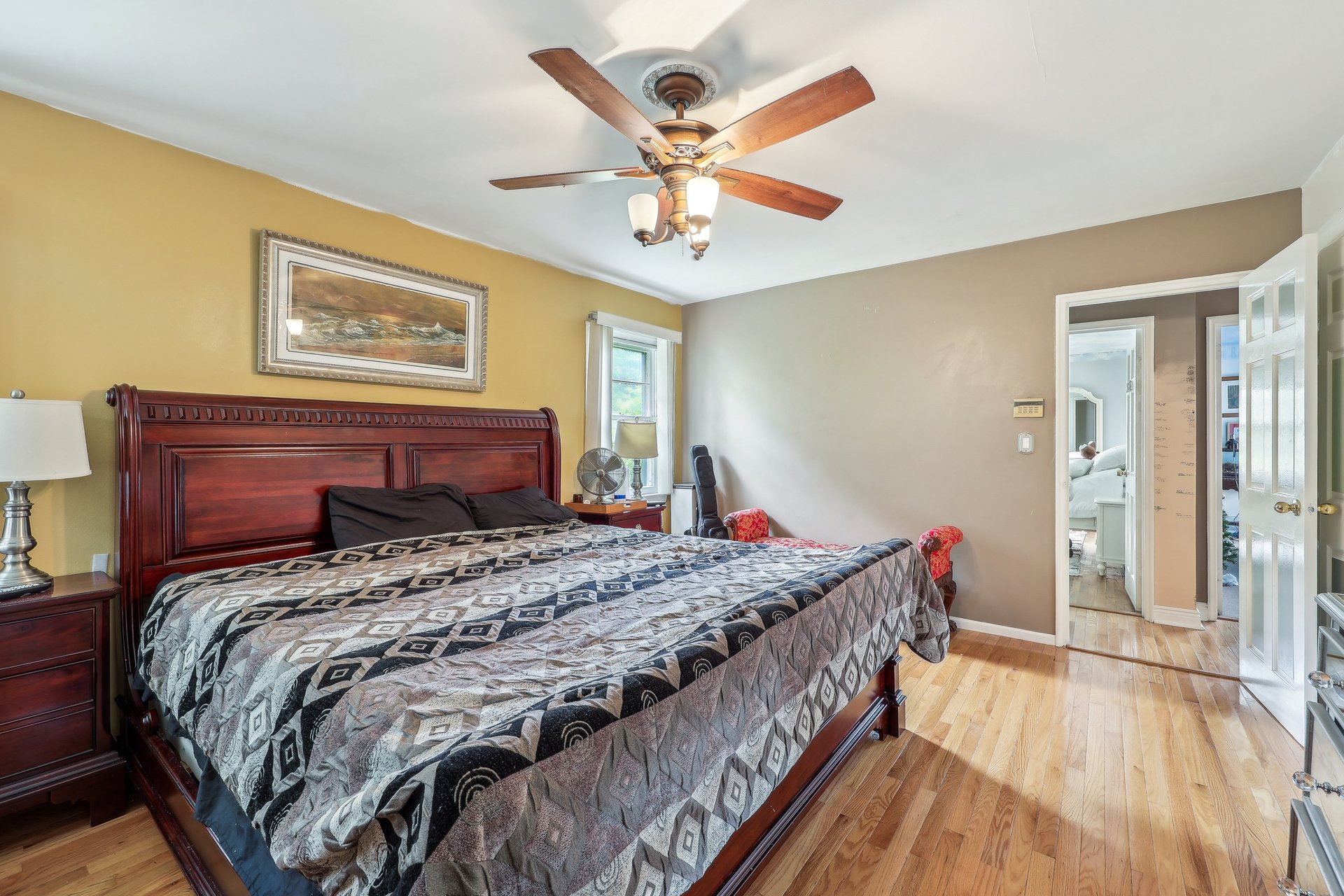 Furnished bedroom with a dark wood bed, patterned quilt, hardwood floors, and a wooden-blade ceiling fan.