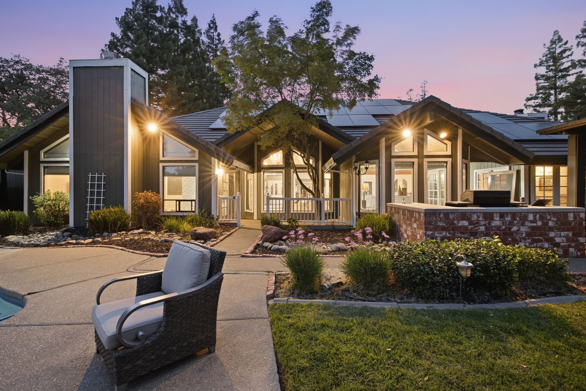 Contemporary home exterior at dusk with solar panels, pool, landscaped patio, and outdoor seating.