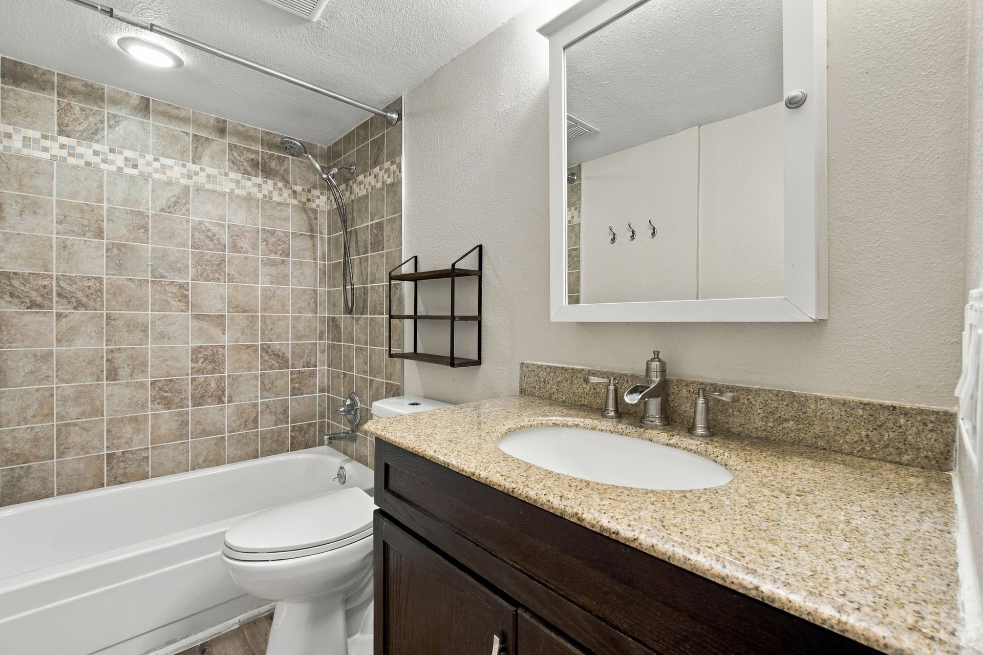 Bathroom with a tiled tub and shower, dark wood vanity, and speckled granite countertop.