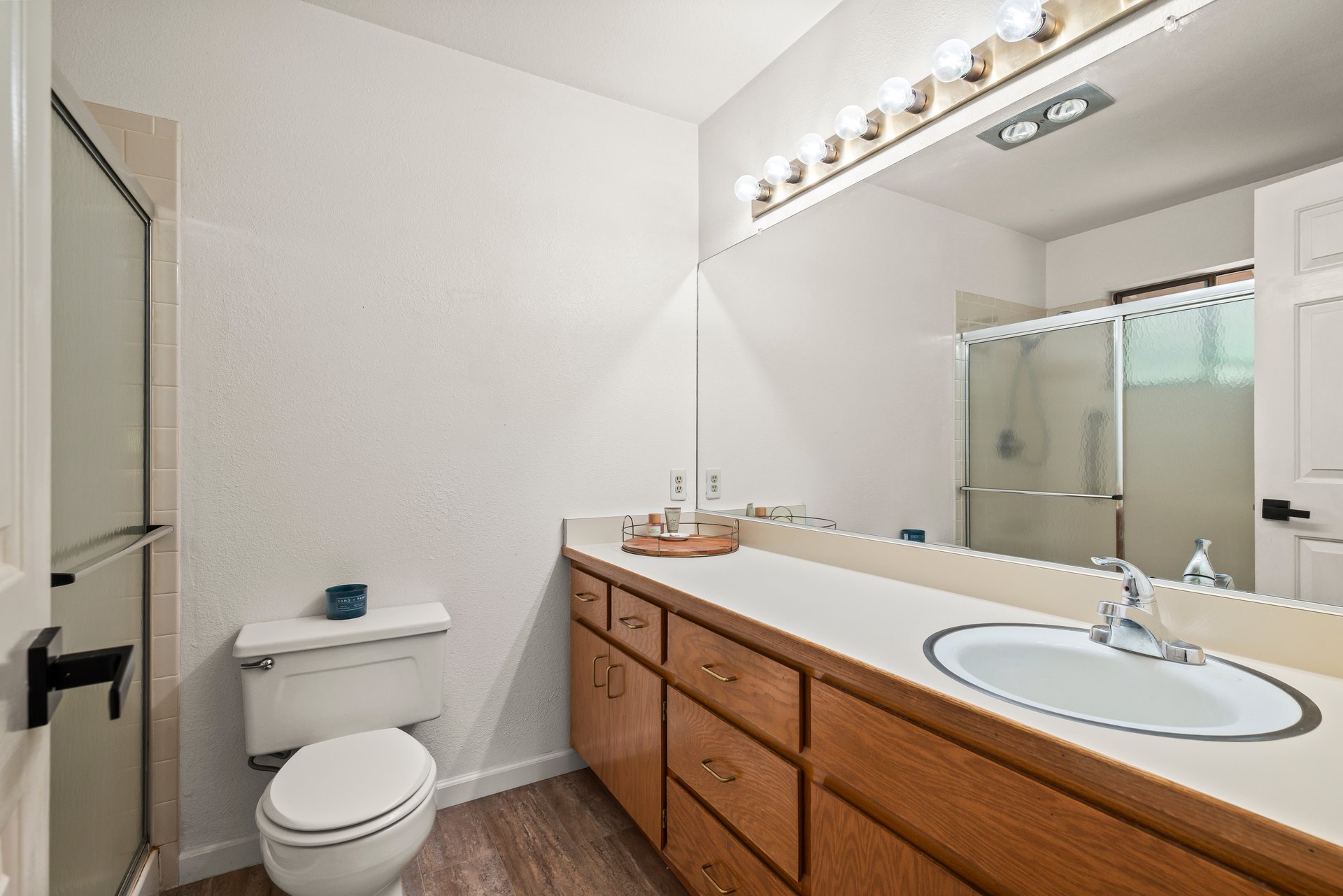 Bathroom with a long wood vanity, oval sink, and sliding glass shower.