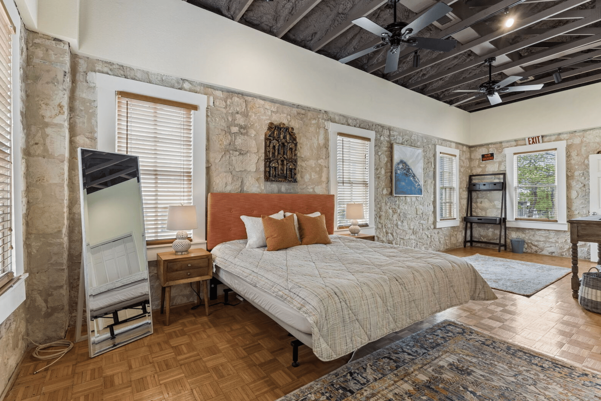 Bedroom with a large bed, exposed stone walls, parquet floors, and an open-beam ceiling.