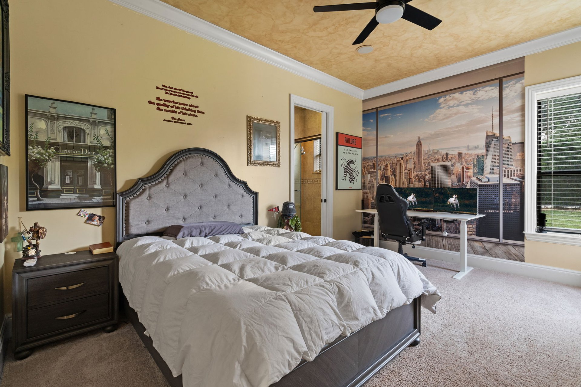 Bedroom with a tufted gray headboard, New York skyline mural, and desk beneath the mural.