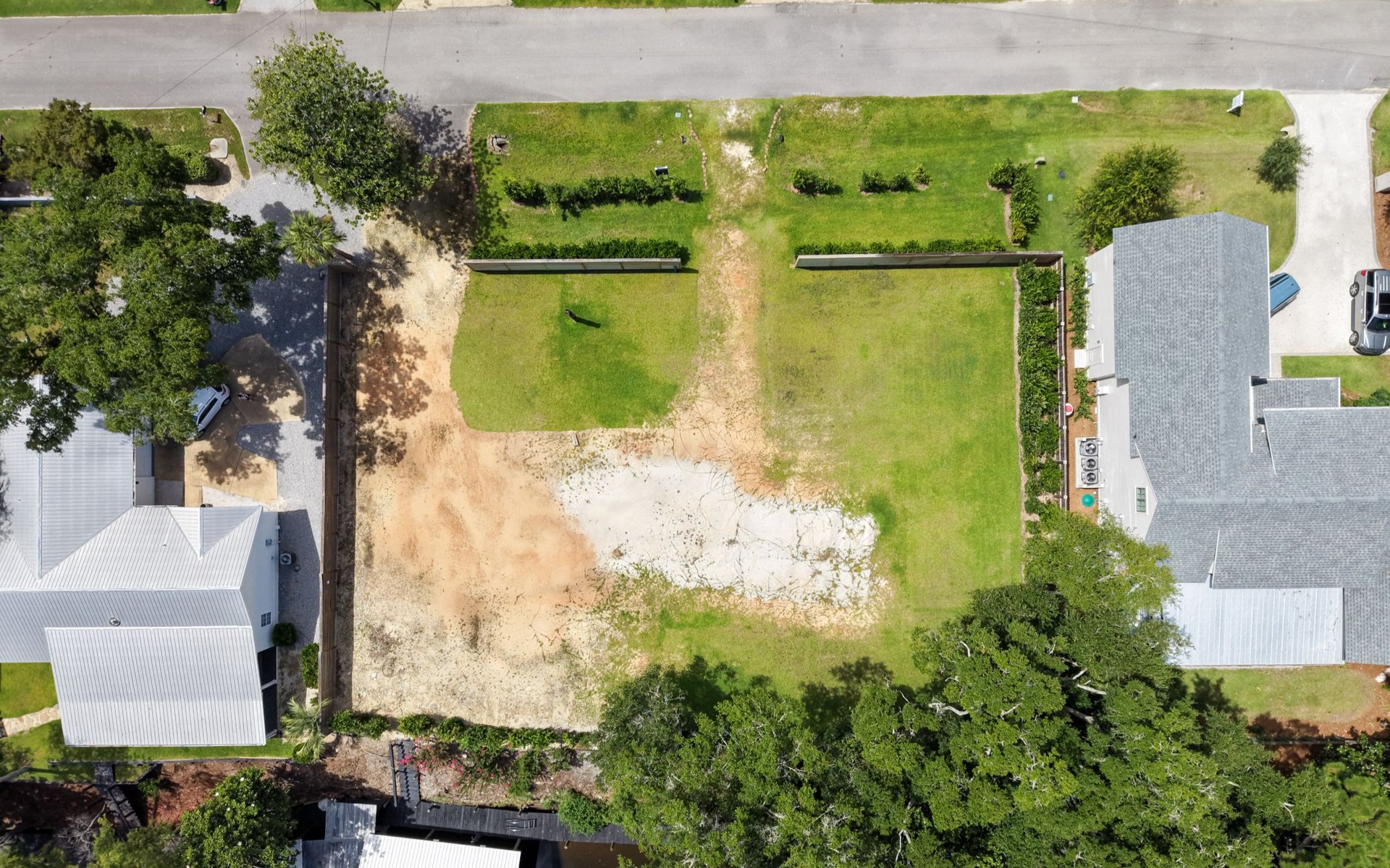 Vacant waterfront lot with a cleared sandy area and a dock beside neighboring homes.