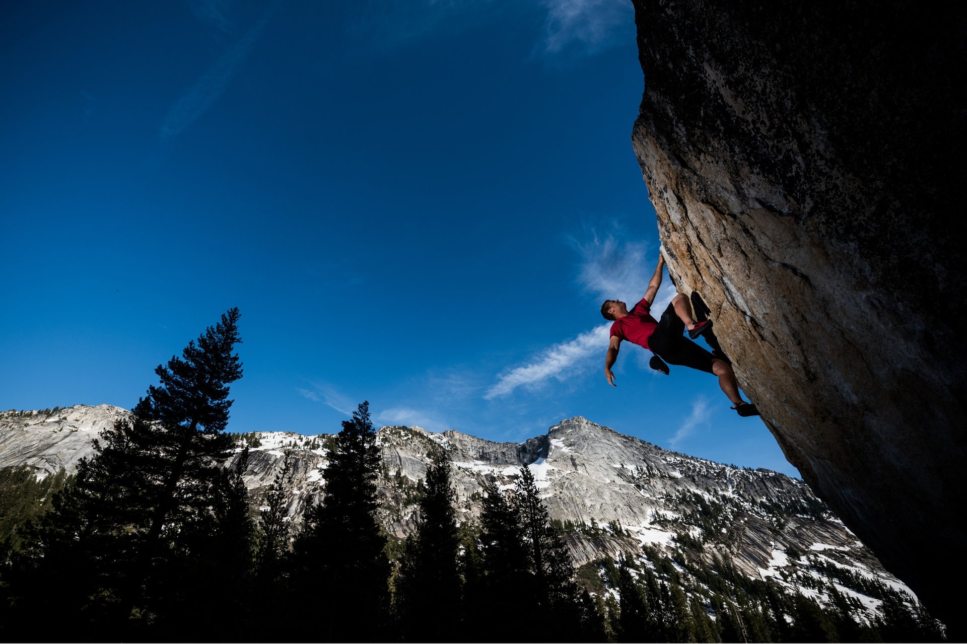 Rock climber on a granite cliff above Yosemite’s pine forest and mountain peaks.