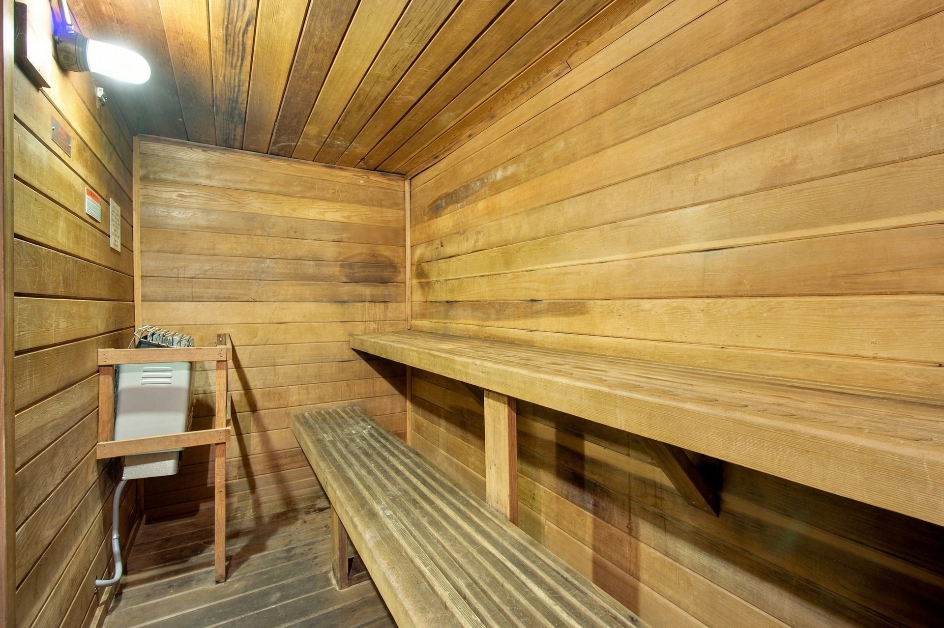 Wood-paneled sauna with tiered benches and a heater in the corner.