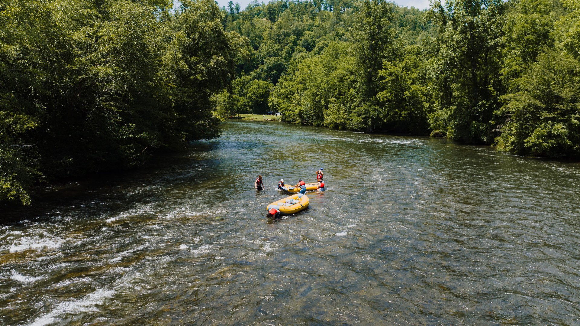 Rafters paddle yellow inflatable boats through a forested river.