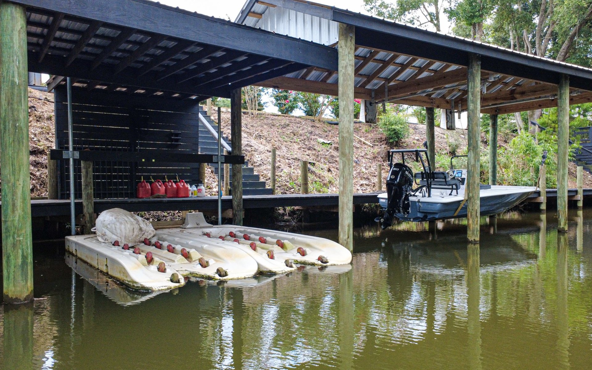 Covered waterfront dock with a motorboat and white pedal boats on the water.