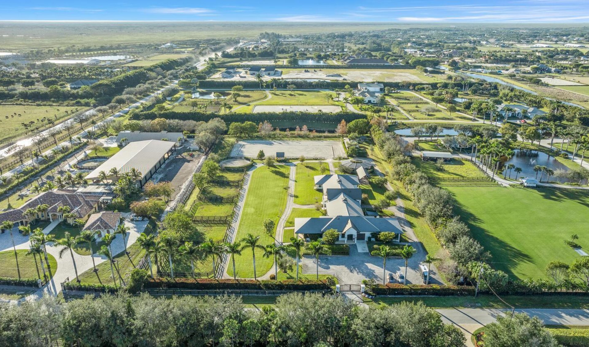 Aerial view of an equestrian estate with fenced paddocks, a riding arena, stable buildings, and a pond.