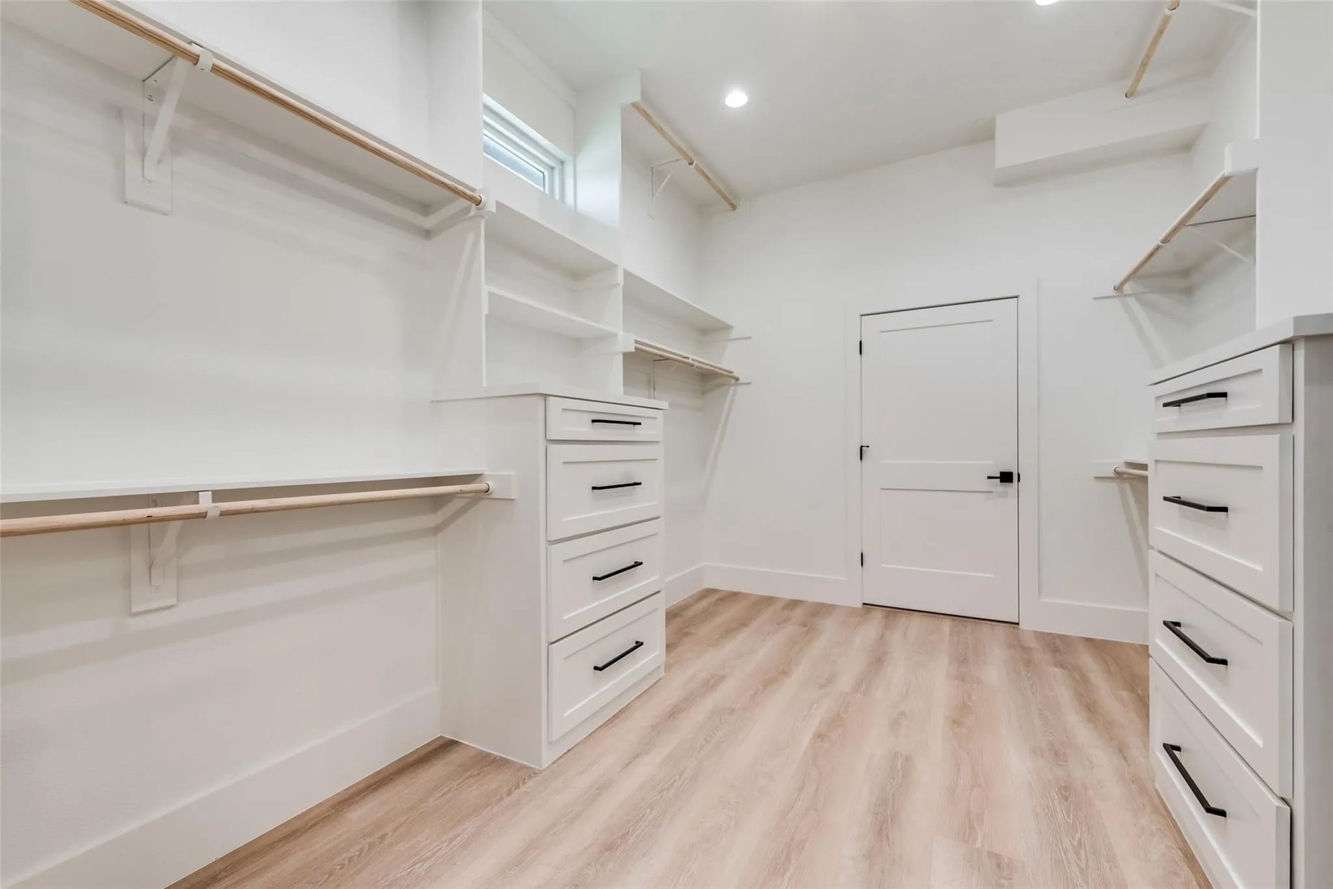 Walk-in closet with white built-in drawers, open shelving, and hanging rods.