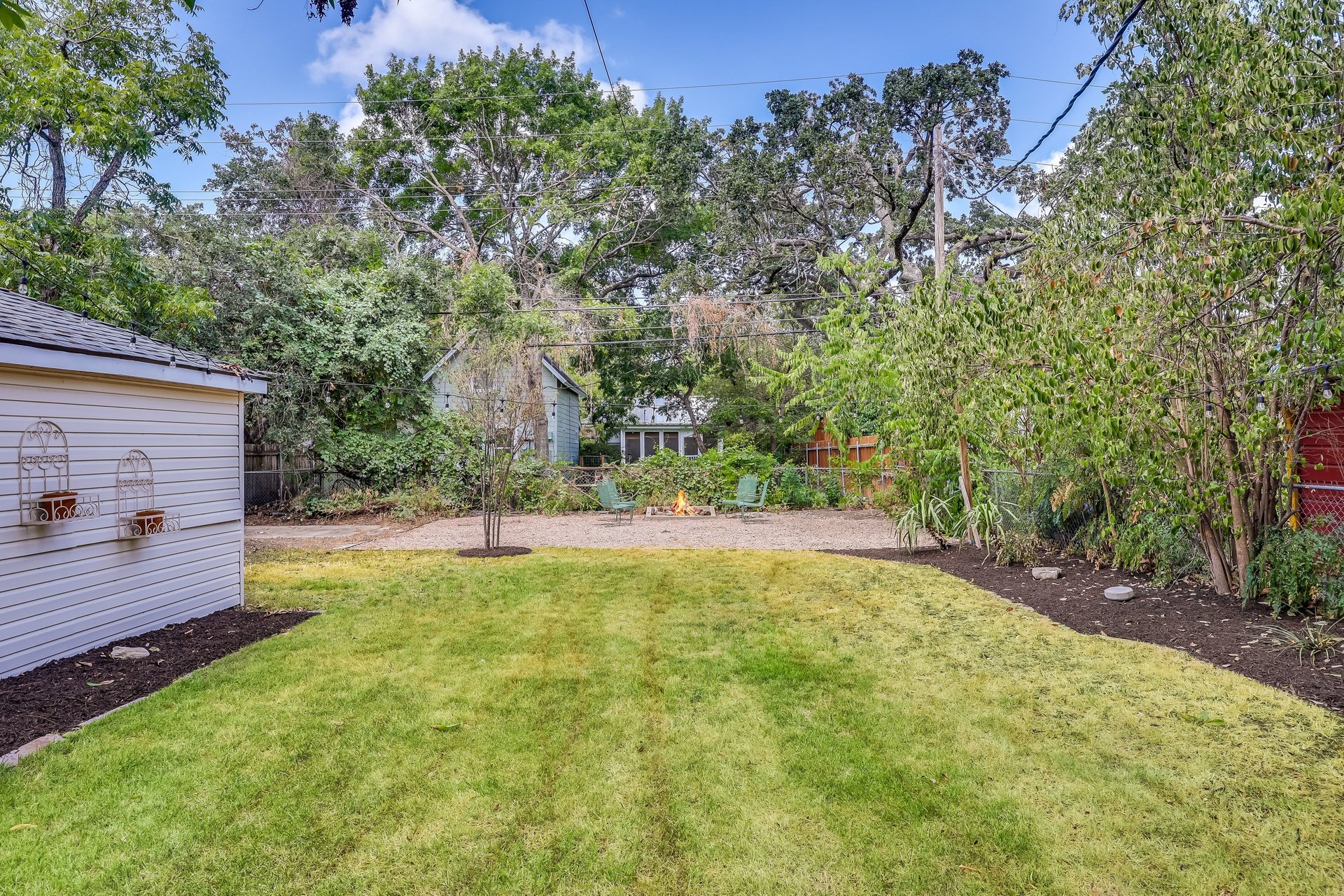 Backyard with a broad lawn, garden shed, and fire pit seating beneath mature trees.