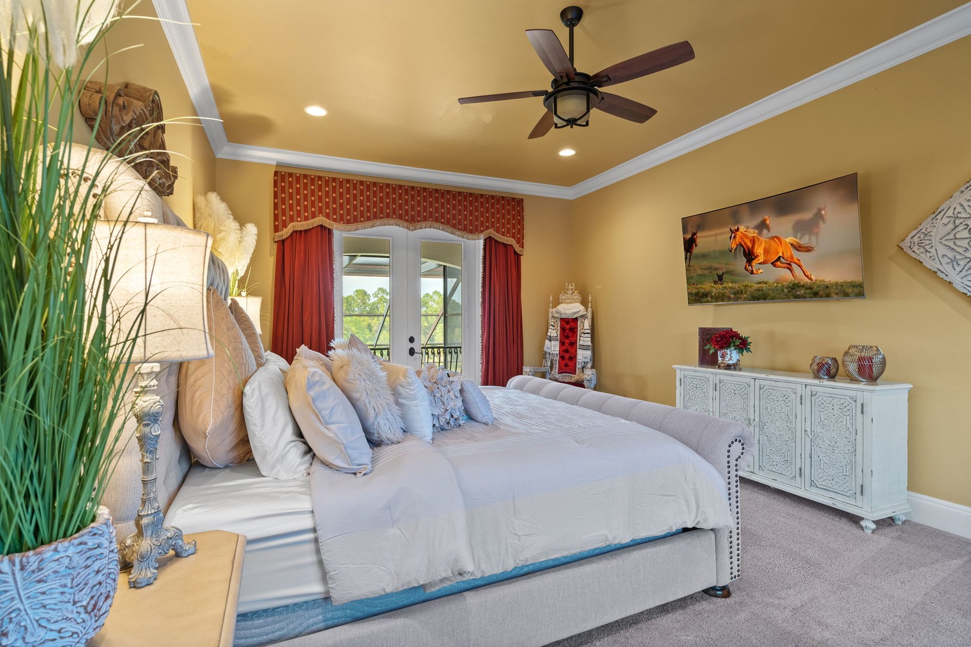 Bedroom with a large pale upholstered bed, red curtains, and a white carved sideboard.