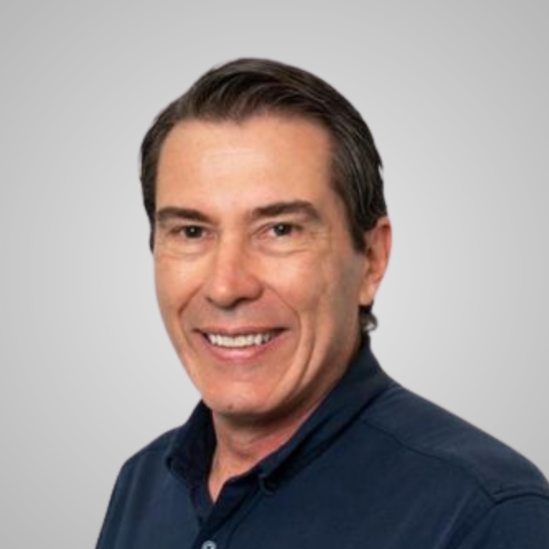 Smiling man in a navy collared shirt against a light gray background.