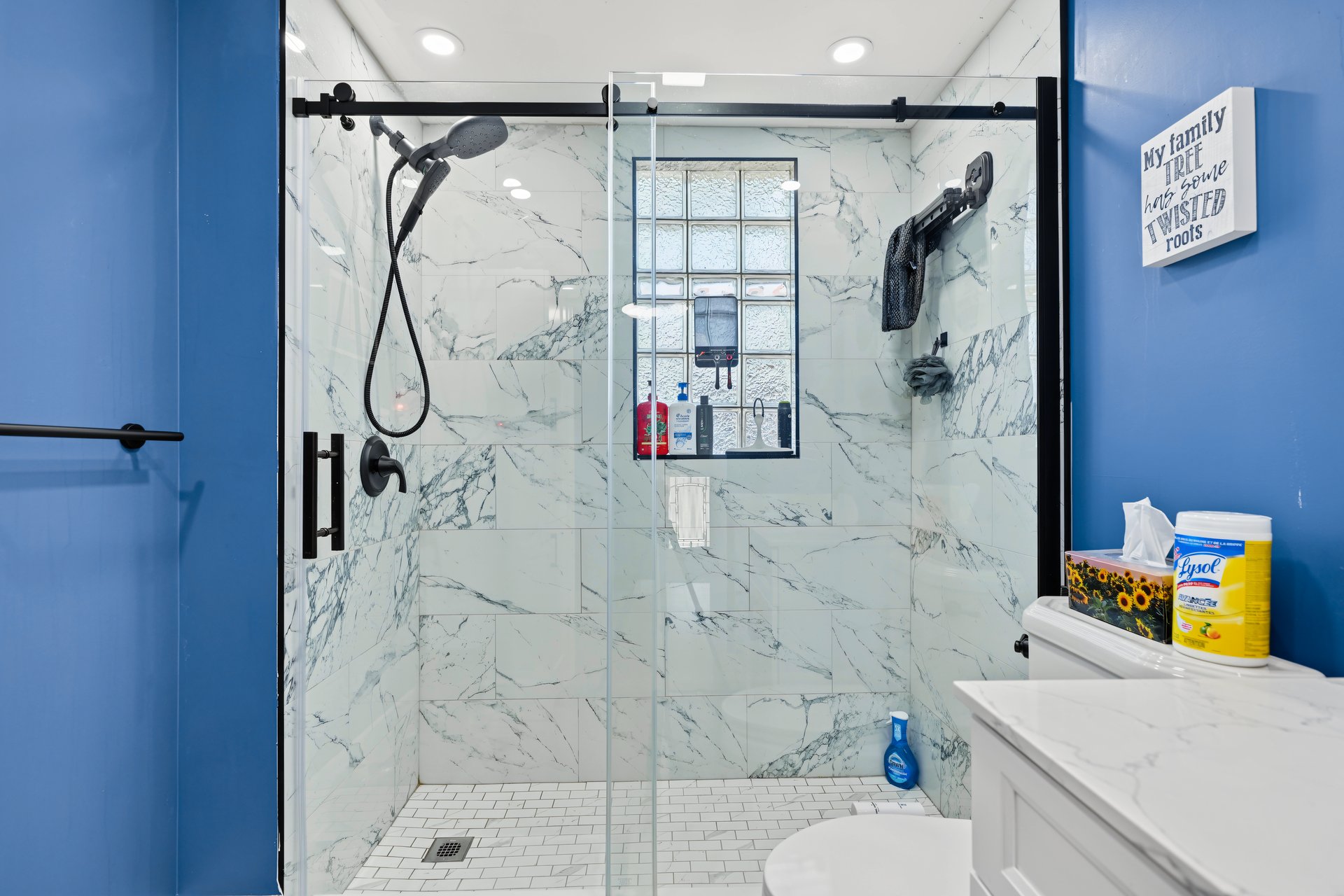 Bathroom with a marble-look walk-in shower, black fixtures, and blue walls.