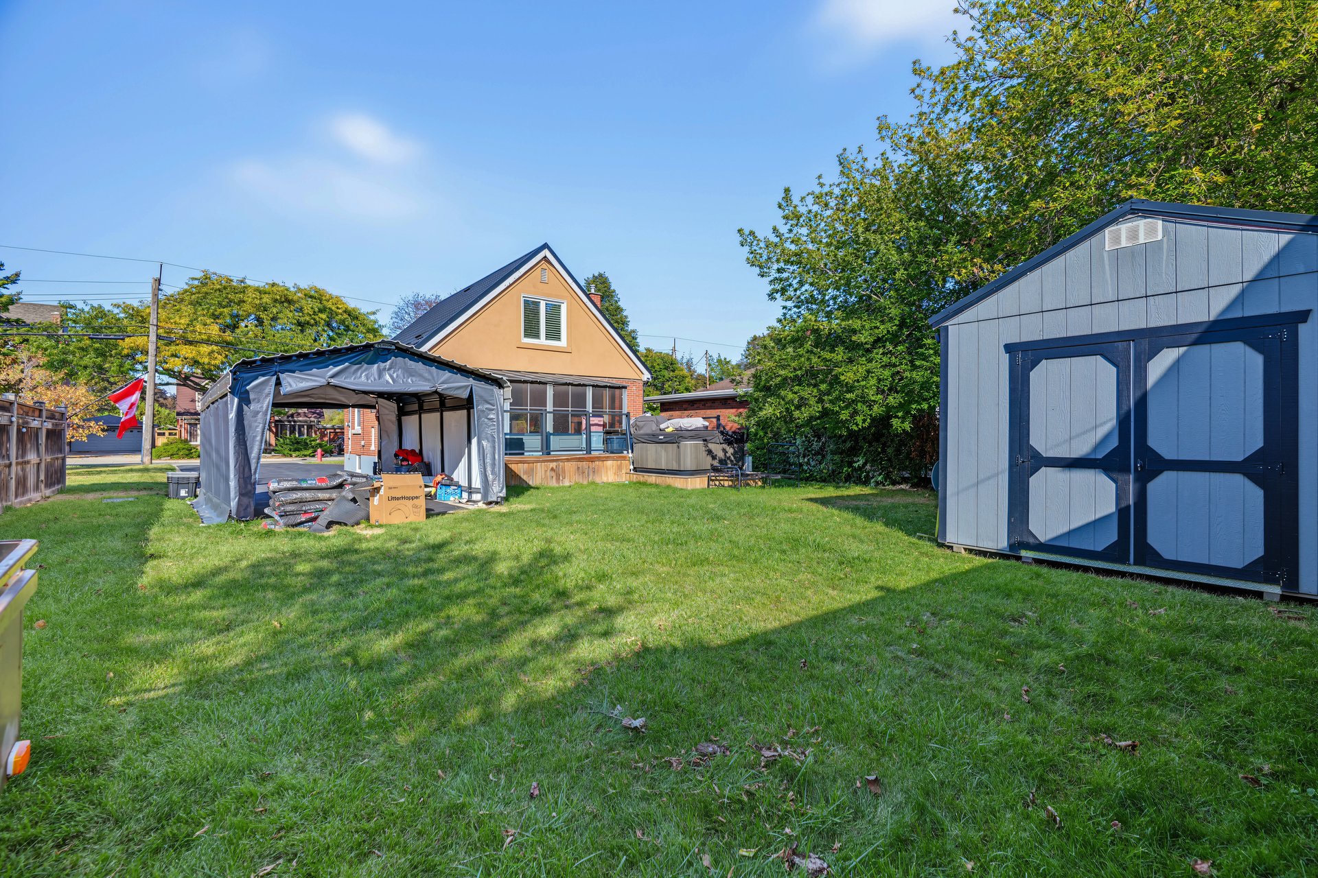 Backyard with a broad lawn, covered canopy, hot tub, and large blue storage shed.