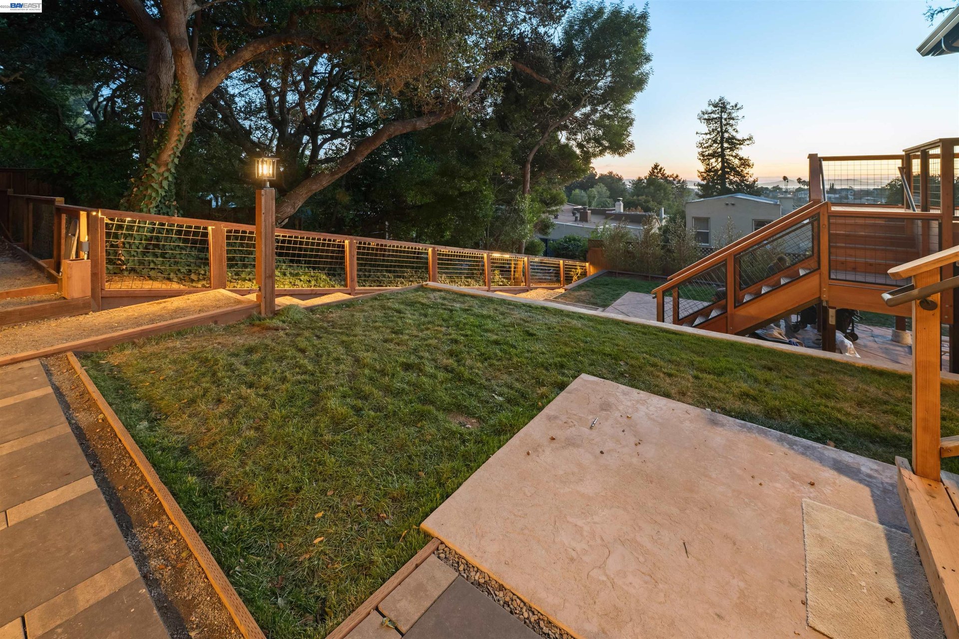 Oakland home's backyard with a broad lawn, stone paths, and wooden deck railings at sunset.