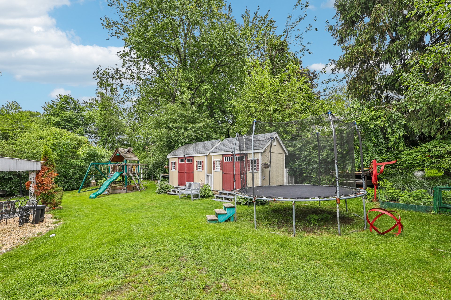 Backyard with red-doored sheds, a trampoline, and a children's playset with a slide.