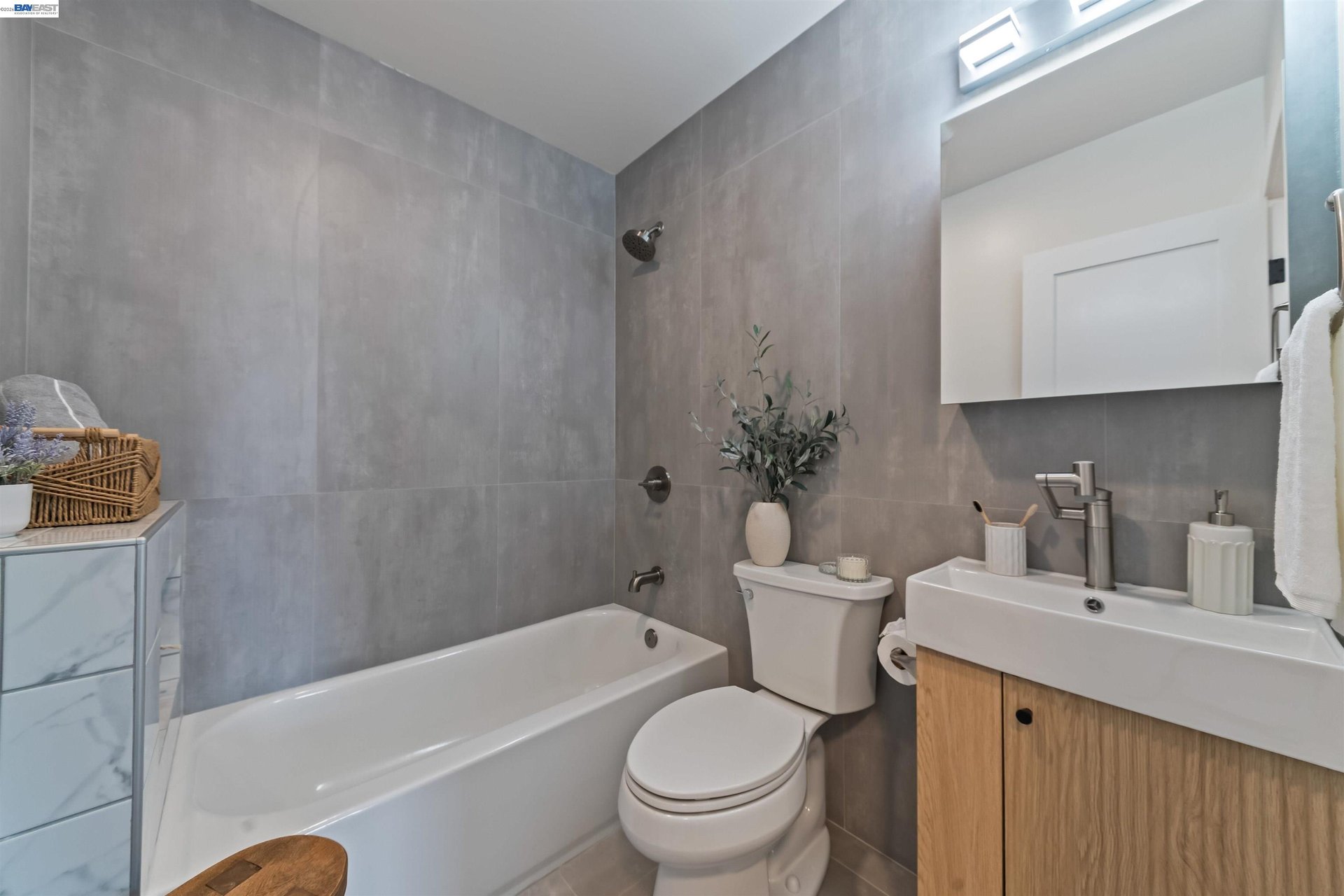 Modern bathroom with gray tile, a white tub, and a wood-front vanity beneath a skylight.