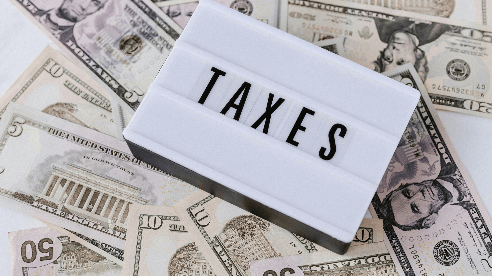 TAXES sign placed over scattered US dollar bills of various denominations