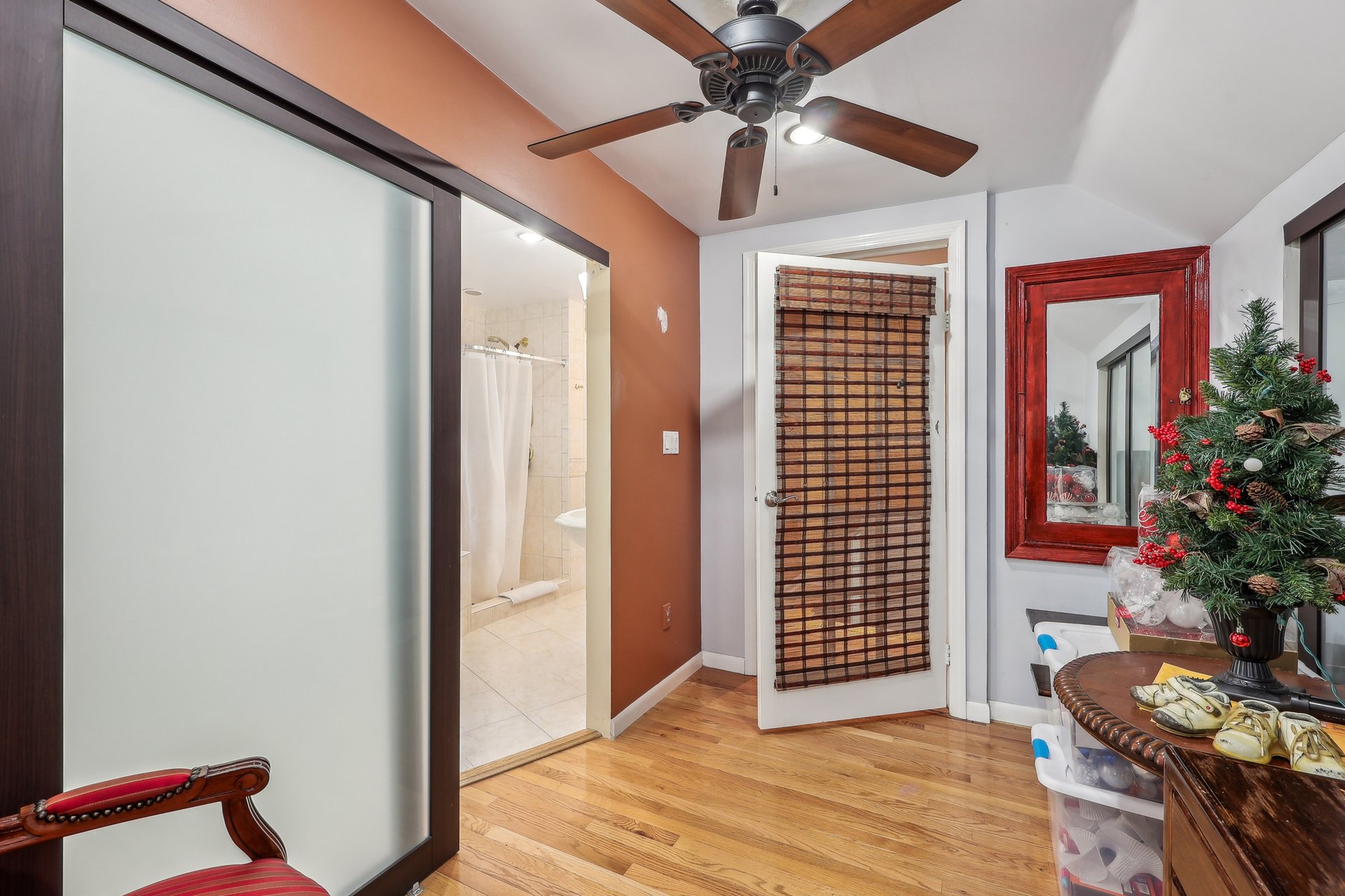 Bathroom with a frosted-glass shower enclosure, hardwood flooring, ceiling fan, and red-framed mirror.