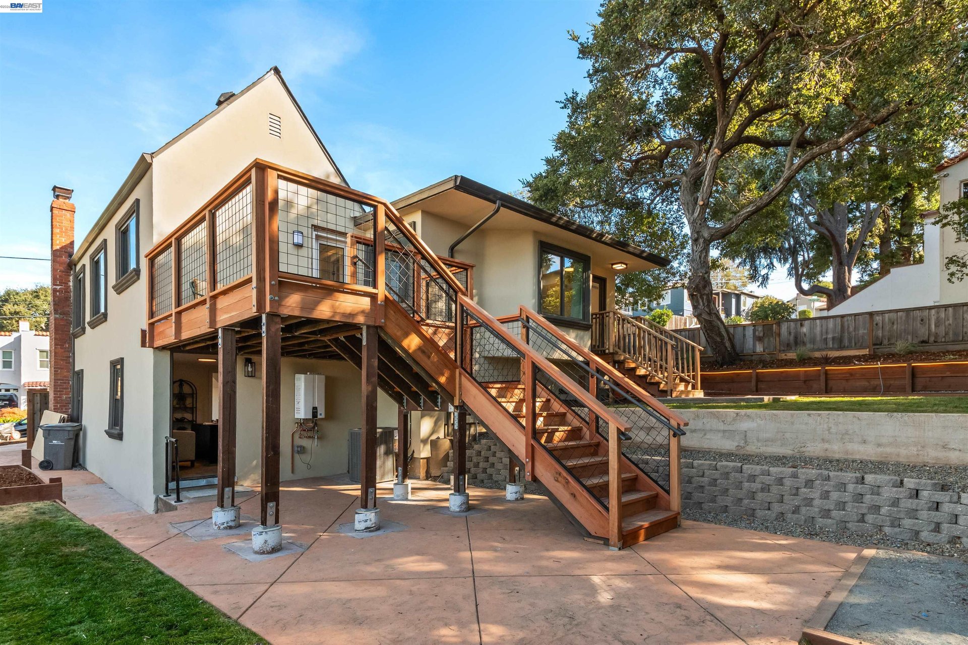 Home’s rear exterior with a raised wooden deck, long staircase, and mature tree in the backyard.