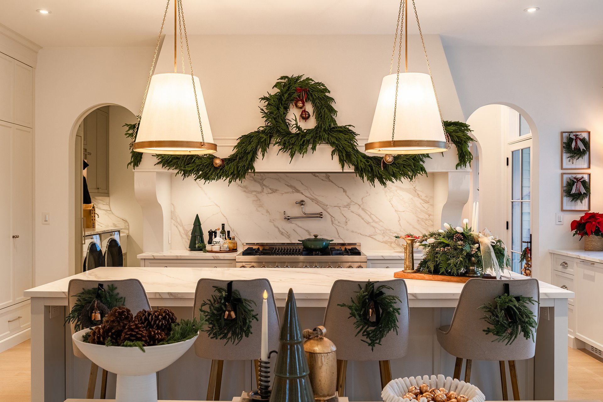 Holiday-styled kitchen island in an Oakville custom home with oversized pendants, marble counters, and greenery wreaths on the bar stools.